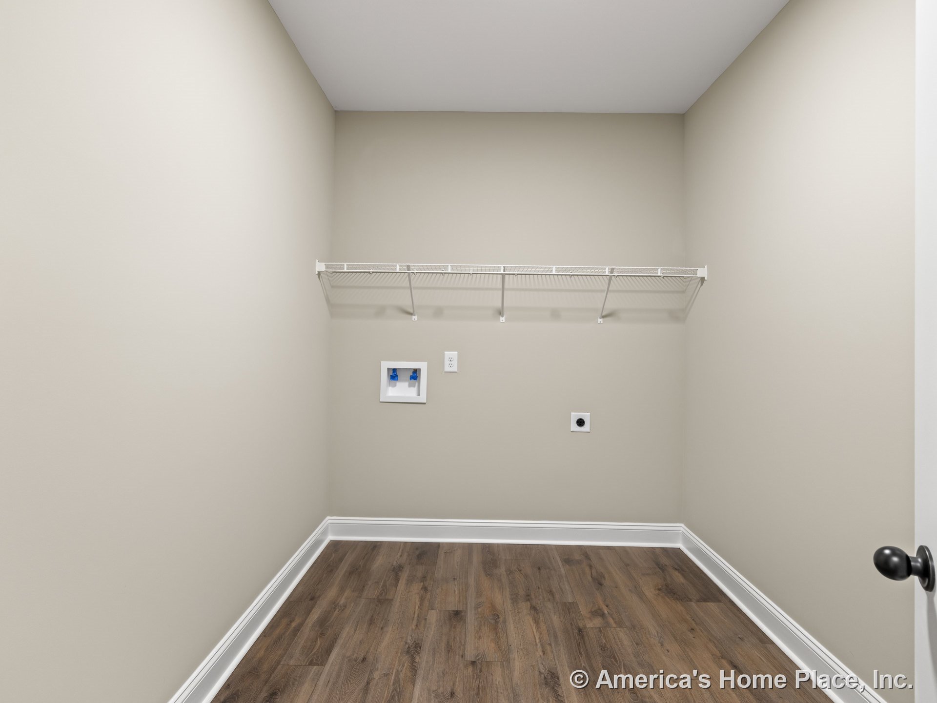 Laundry room with wire shelving above washer and dryer hookups, wood-look flooring, neutral walls, white baseboards, flat ceiling, door hardware, and wall outlet.