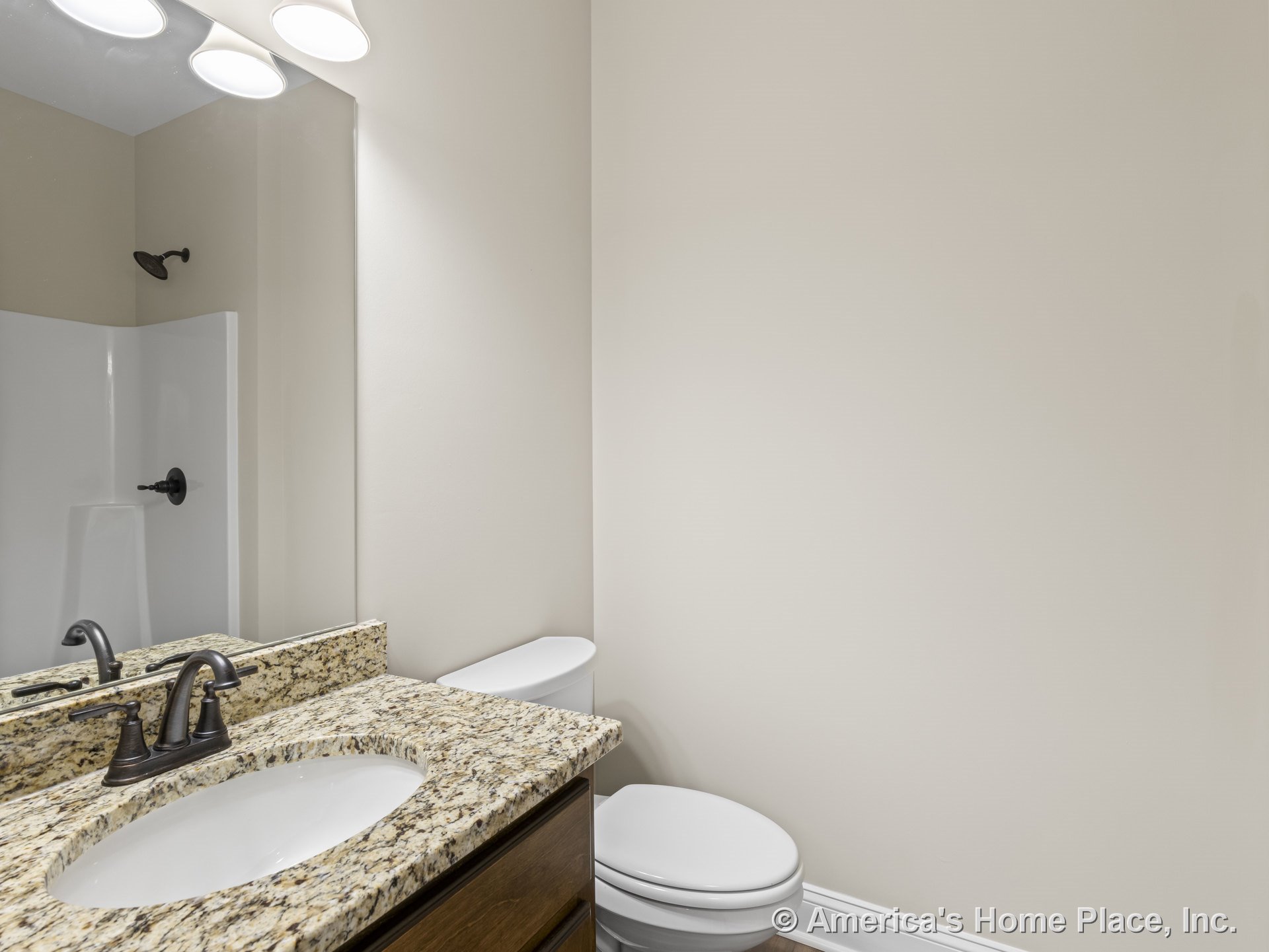 Granite vanity with undermount sink and bronze faucet, wall-mounted mirror above, white toilet adjacent, shower with dark hardware, neutral wall color, cabinetry, and trim.
