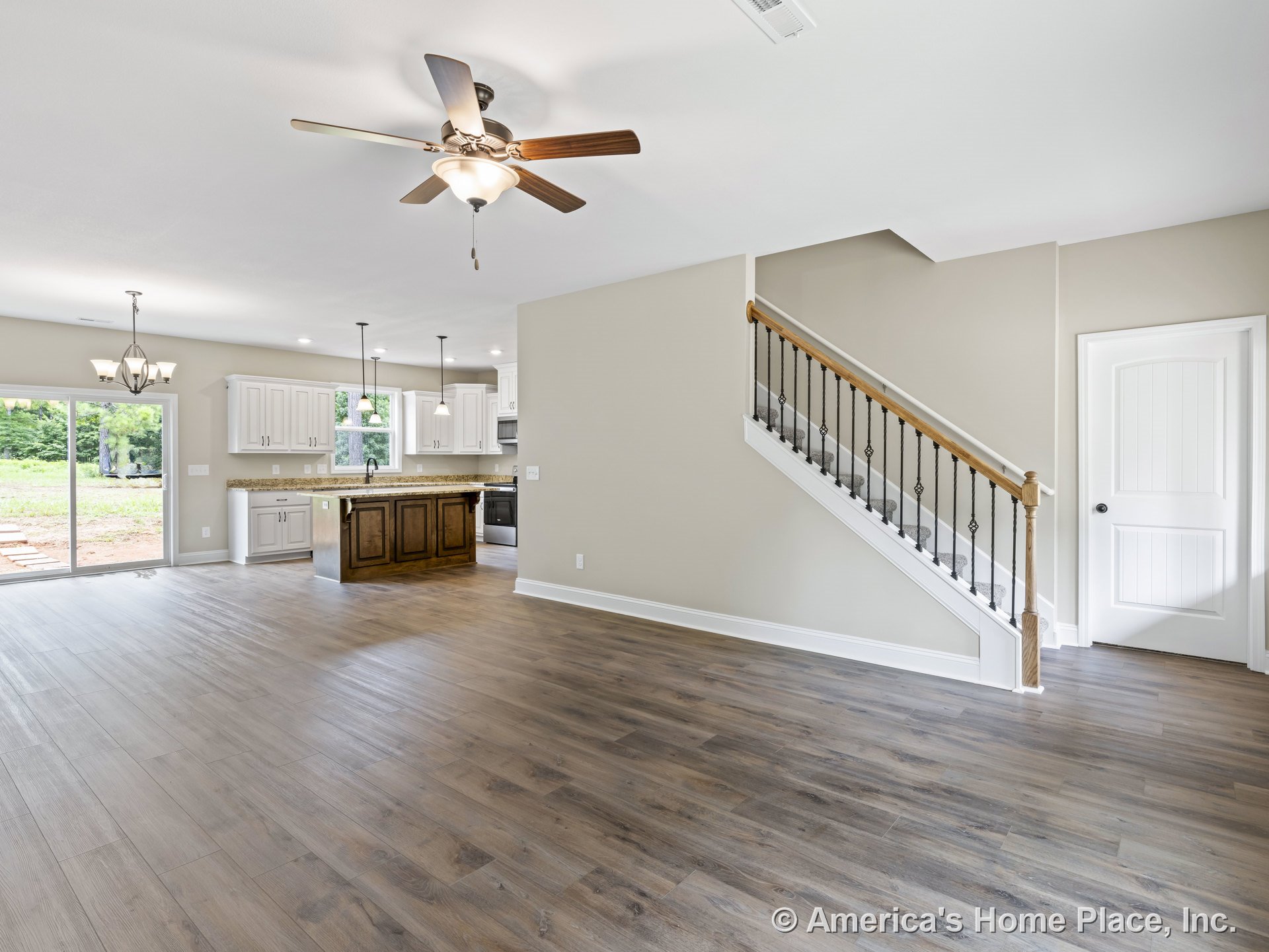 Open concept living area with wood-look plank flooring, staircase featuring iron balusters, kitchen equipped with granite countertops and white upper and lower cabinets, pendant