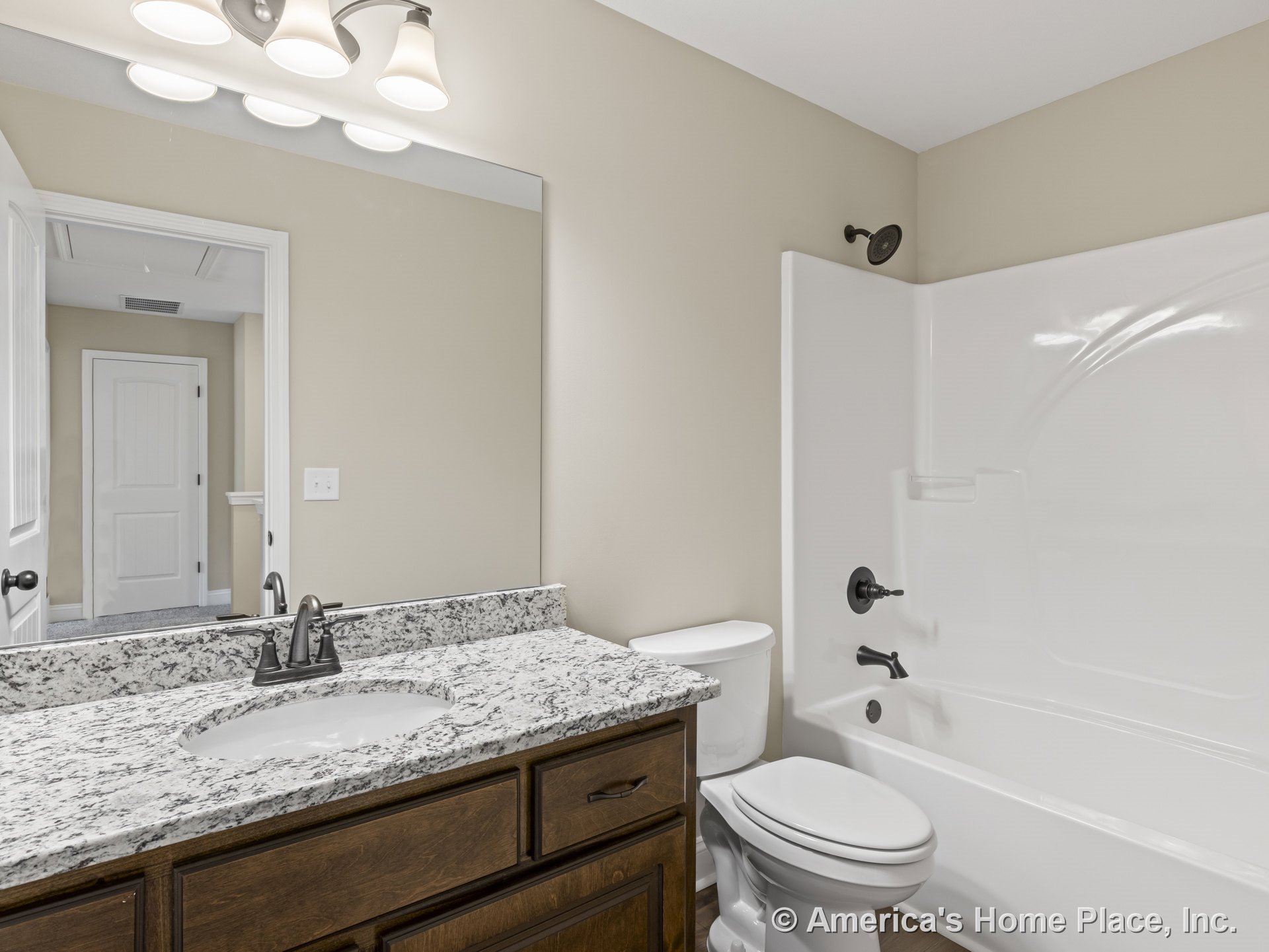 Granite countertop atop wood vanity cabinetry with single sink, wall-mounted mirror, three-light fixture, white fiberglass tub-shower combo, white toilet, neutral painted walls