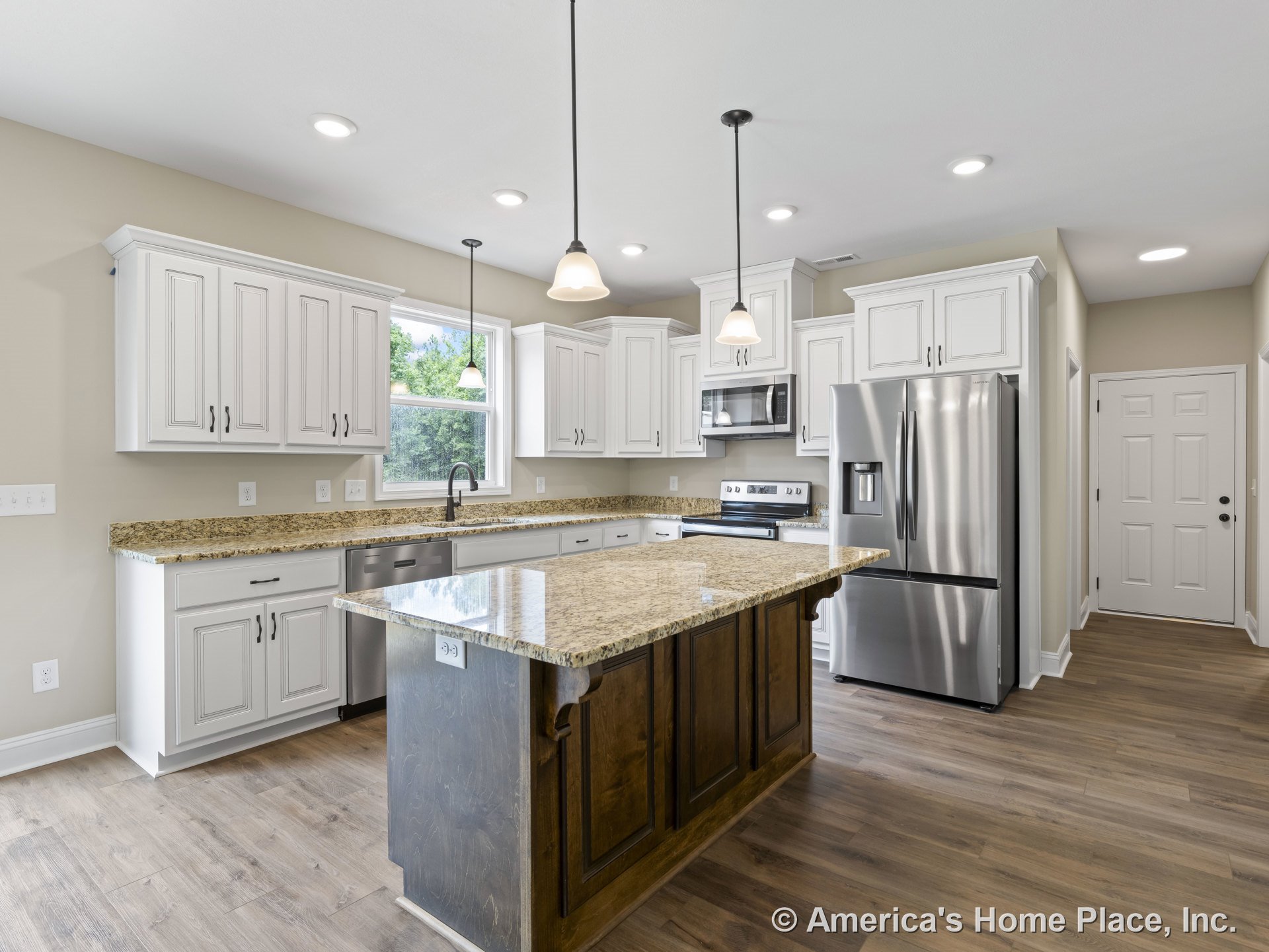 Granite kitchen island with double sink, white raised-panel cabinetry, stainless steel refrigerator and built-in microwave, pendant and recessed lighting, wood-look flooring