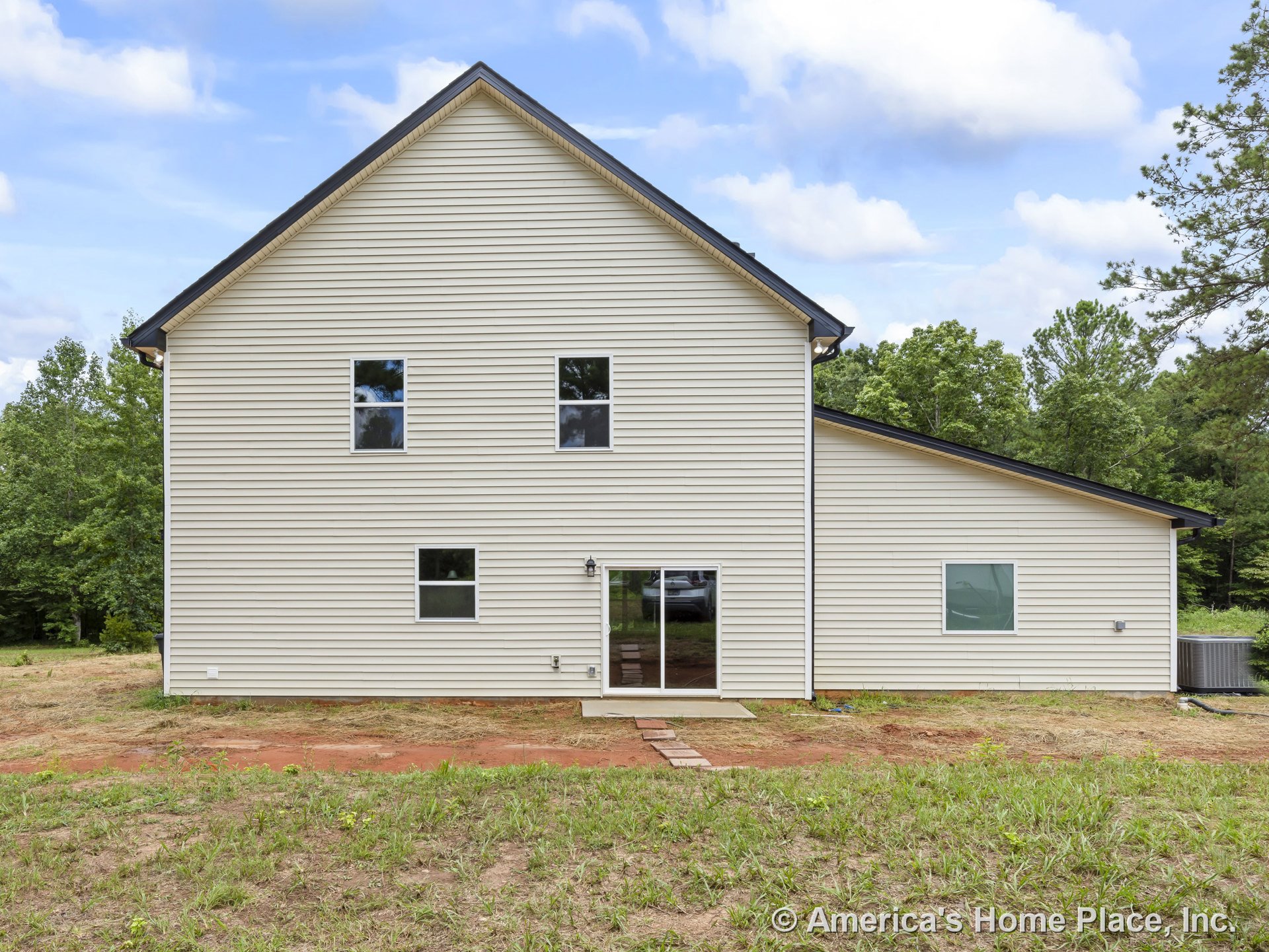Beige horizontal vinyl siding with multiple rectangular windows, sliding glass door, gable roof, outdoor light fixture, and concrete step at entry.