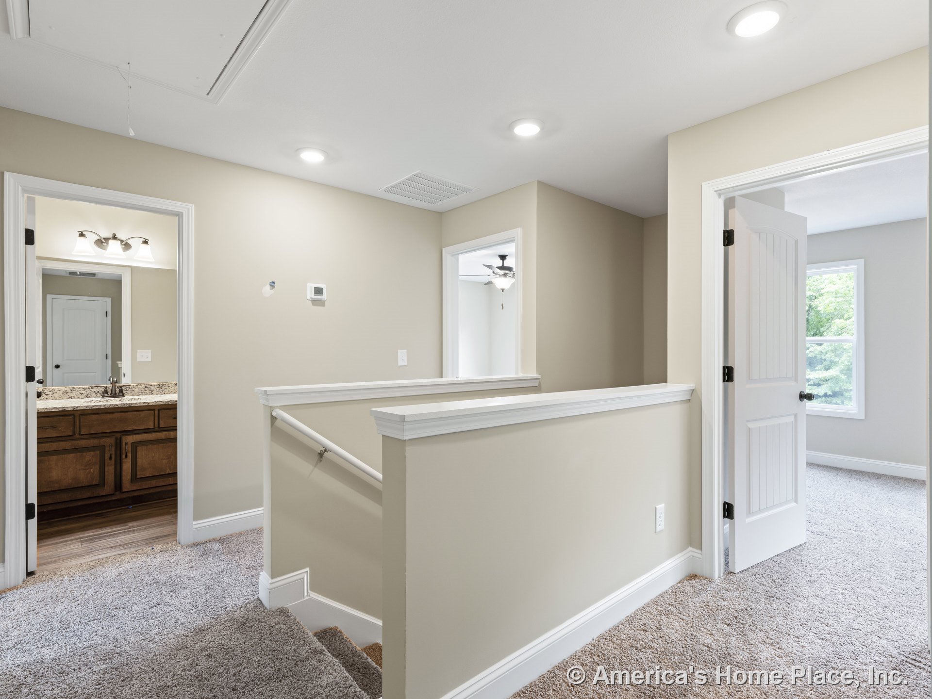 Carpeted upstairs hallway with recessed ceiling lights, white trim and interior doors, stair railing, and access to a bathroom featuring granite countertop, wood vanity cabinetry