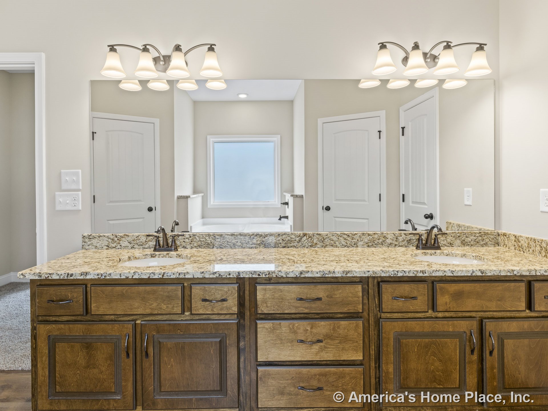 Double vanity with granite countertop, wood cabinetry, two large framed mirrors, built-in lighting fixtures, and paneled doors with trim.