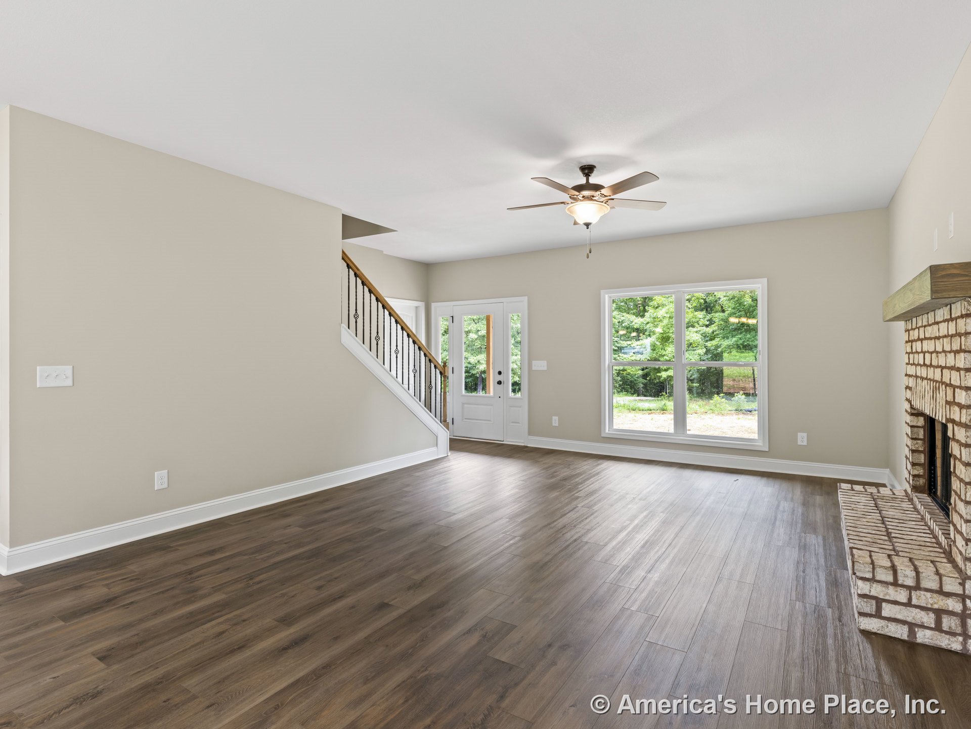 Brick fireplace with raised hearth, double window with white trim, wood plank flooring, ceiling fan with light fixture, staircase featuring iron balusters, neutral painted walls