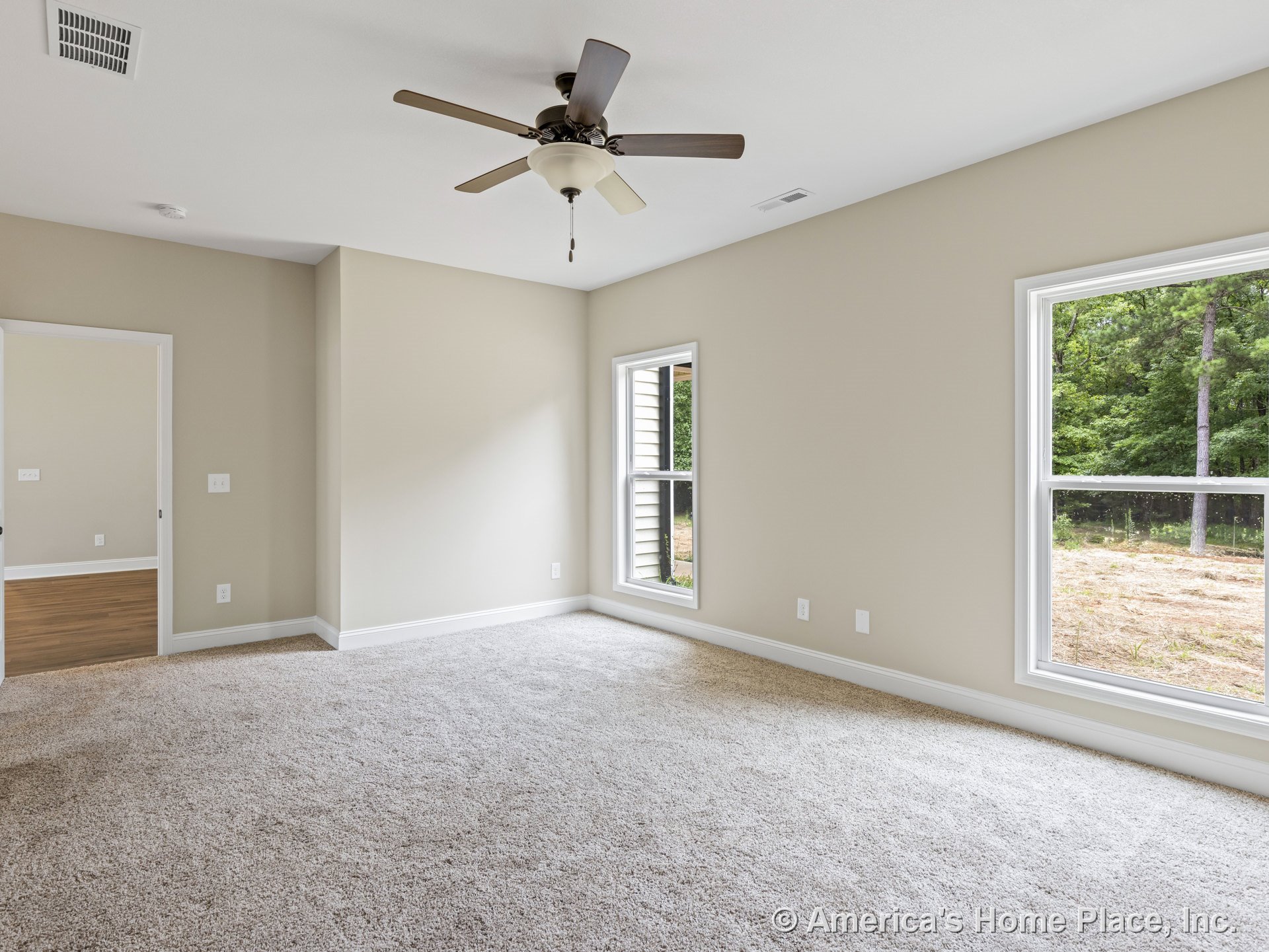 Carpeted bedroom with two large windows, ceiling fan and light fixture, neutral painted walls, white baseboards, and open doorway to adjacent room.