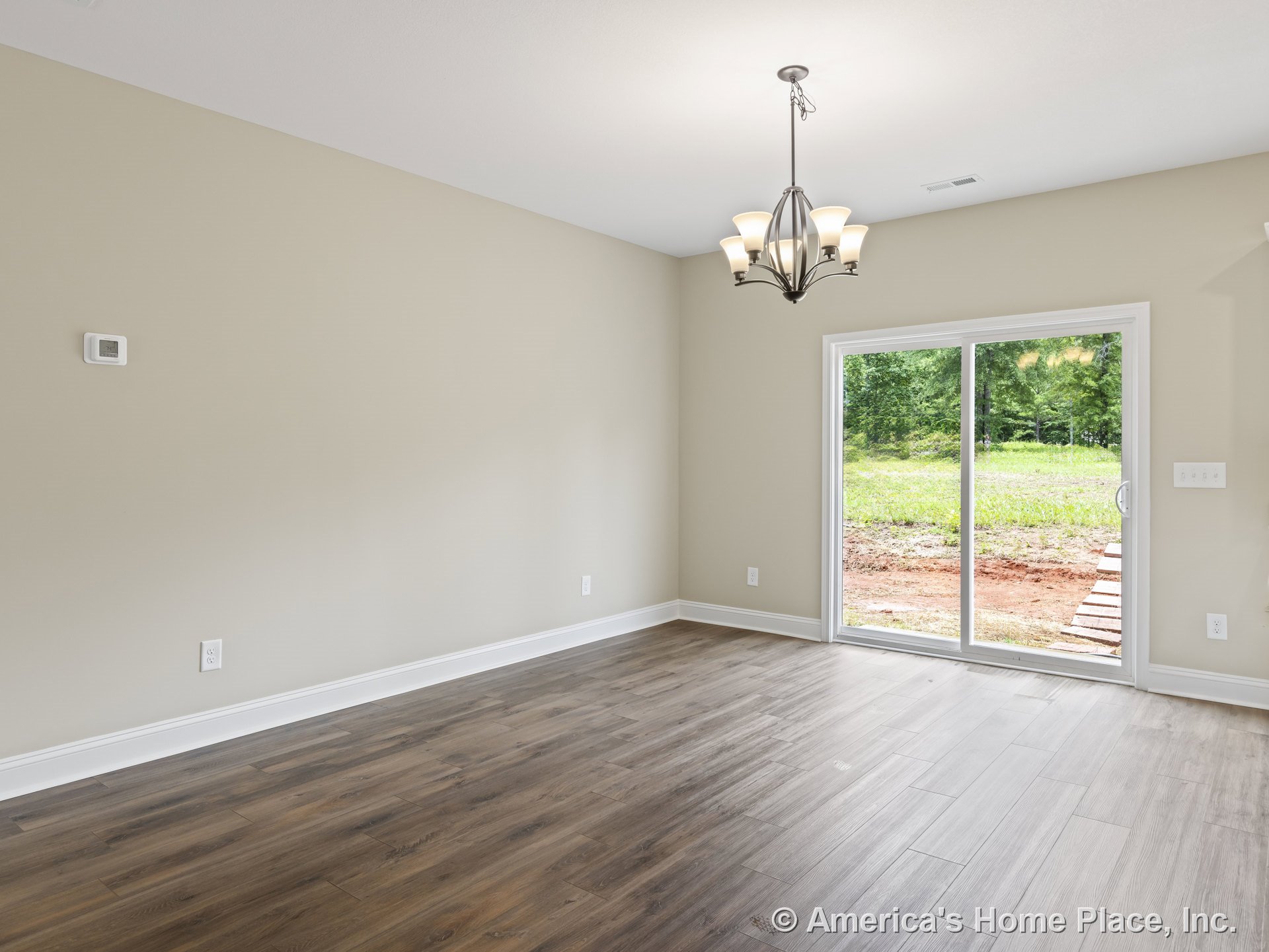 Dining area with wood-look plank flooring, modern chandelier, neutral wall paint, white baseboard trim, sliding glass patio doors opening to backyard, and wall-mounted thermostat.