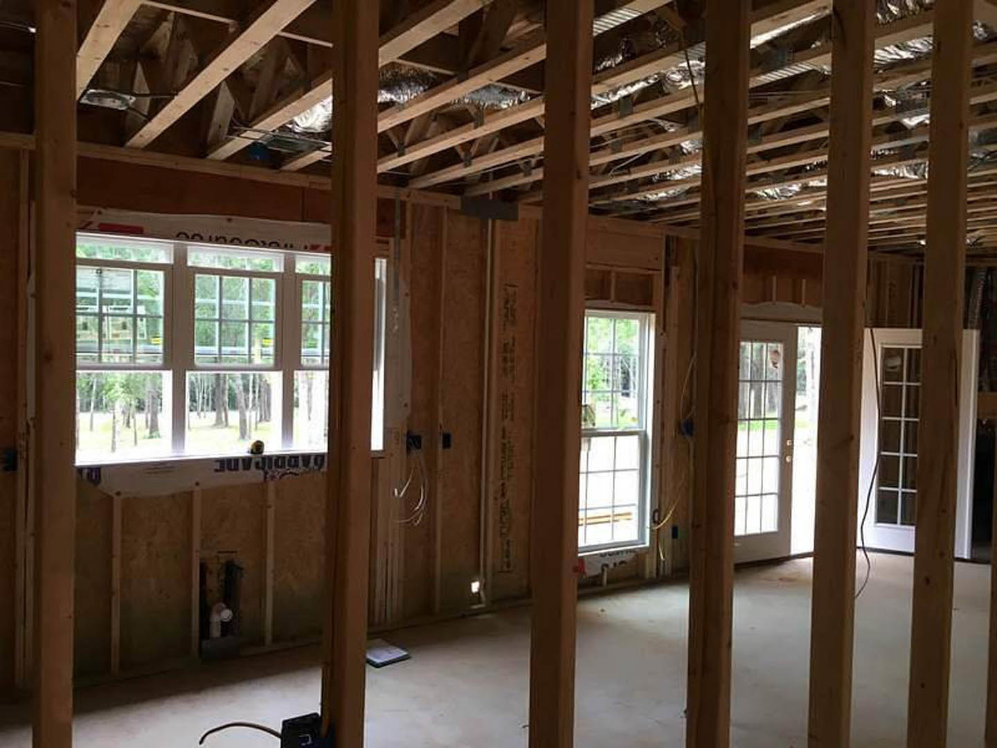 Open-concept room featuring exposed wooden ceiling beams, large windows with glass panes, hardwood flooring, and a glass-paneled door.