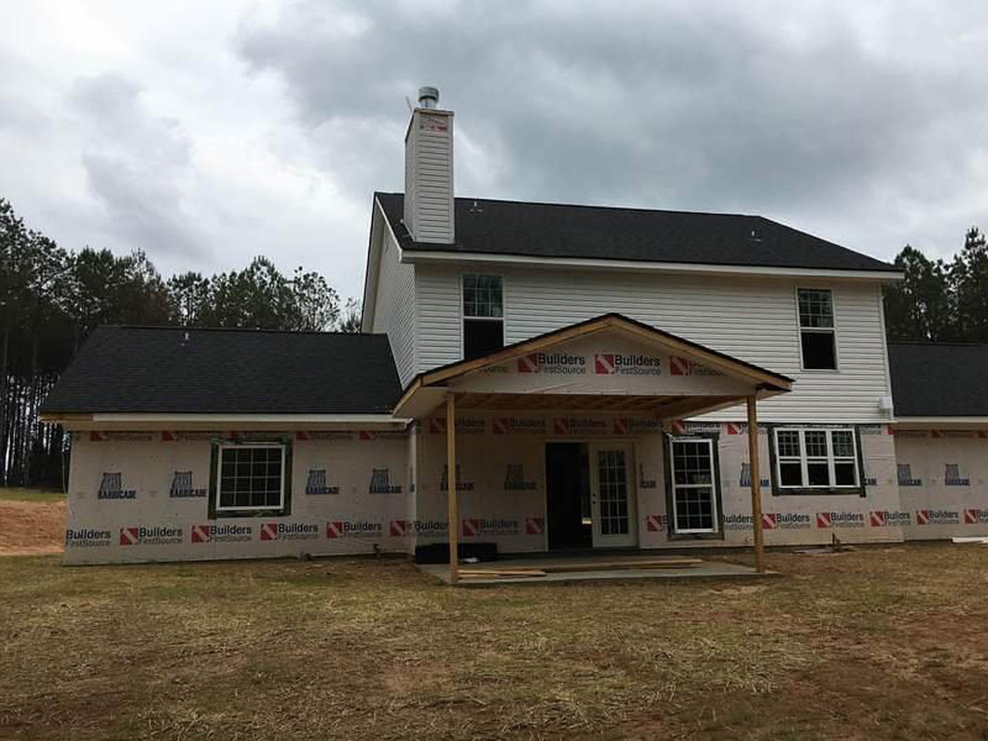 Covered front porch with white columns, black door, grid windows, potted plant on windowsill, light siding, and landscaped yard.
