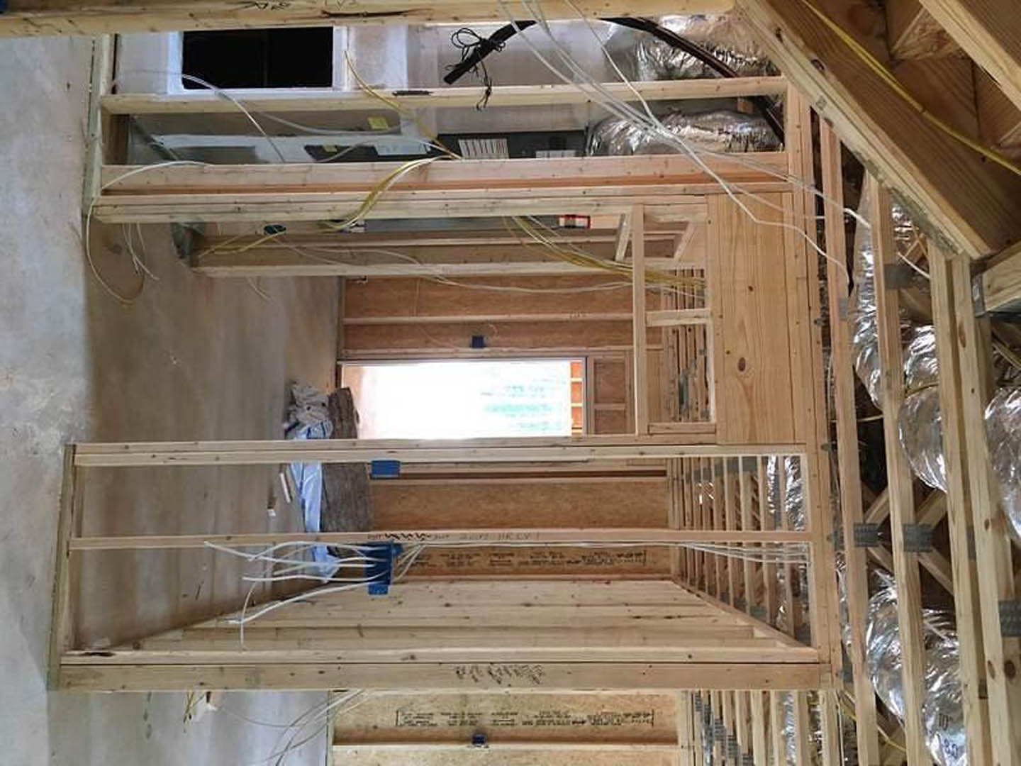 Exposed wood framing and beams inside a house under construction, with unfinished walls and visible building insulation