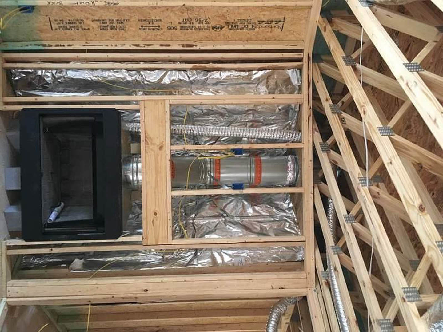 Wood-framed wall with exposed silver pipes, mounted television, and visible lumber beams; black metal safe with rolled paper, heater, microwave, and metal cylinder nearby.