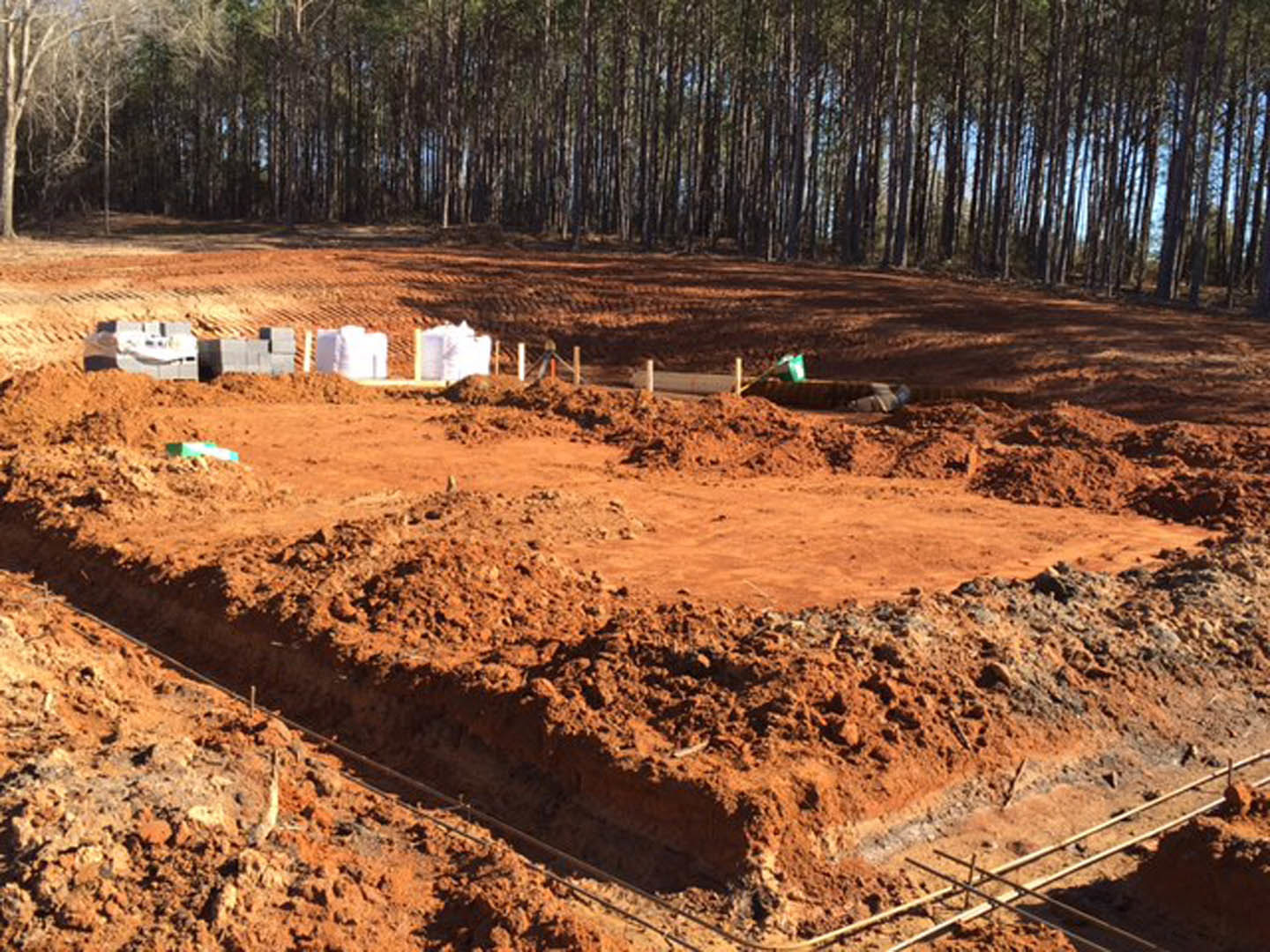 Dirt construction site with exposed soil and tree line in the background, early stage home foundation excavation