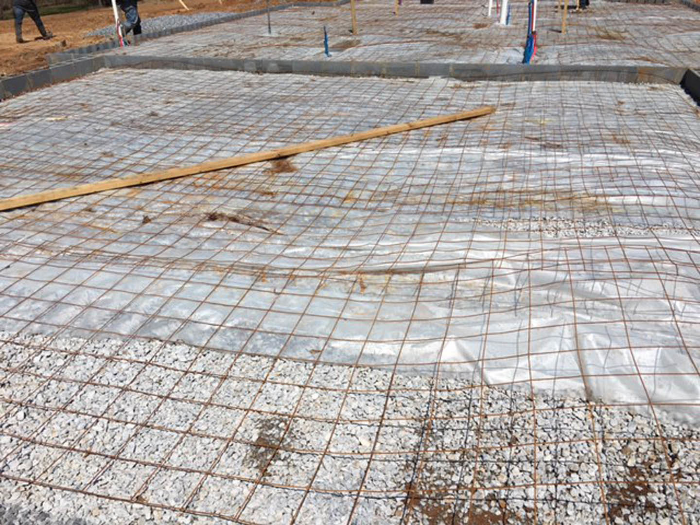 Wire mesh grid laid over a concrete slab outdoors, with dirt and a blurry foot visible in the background