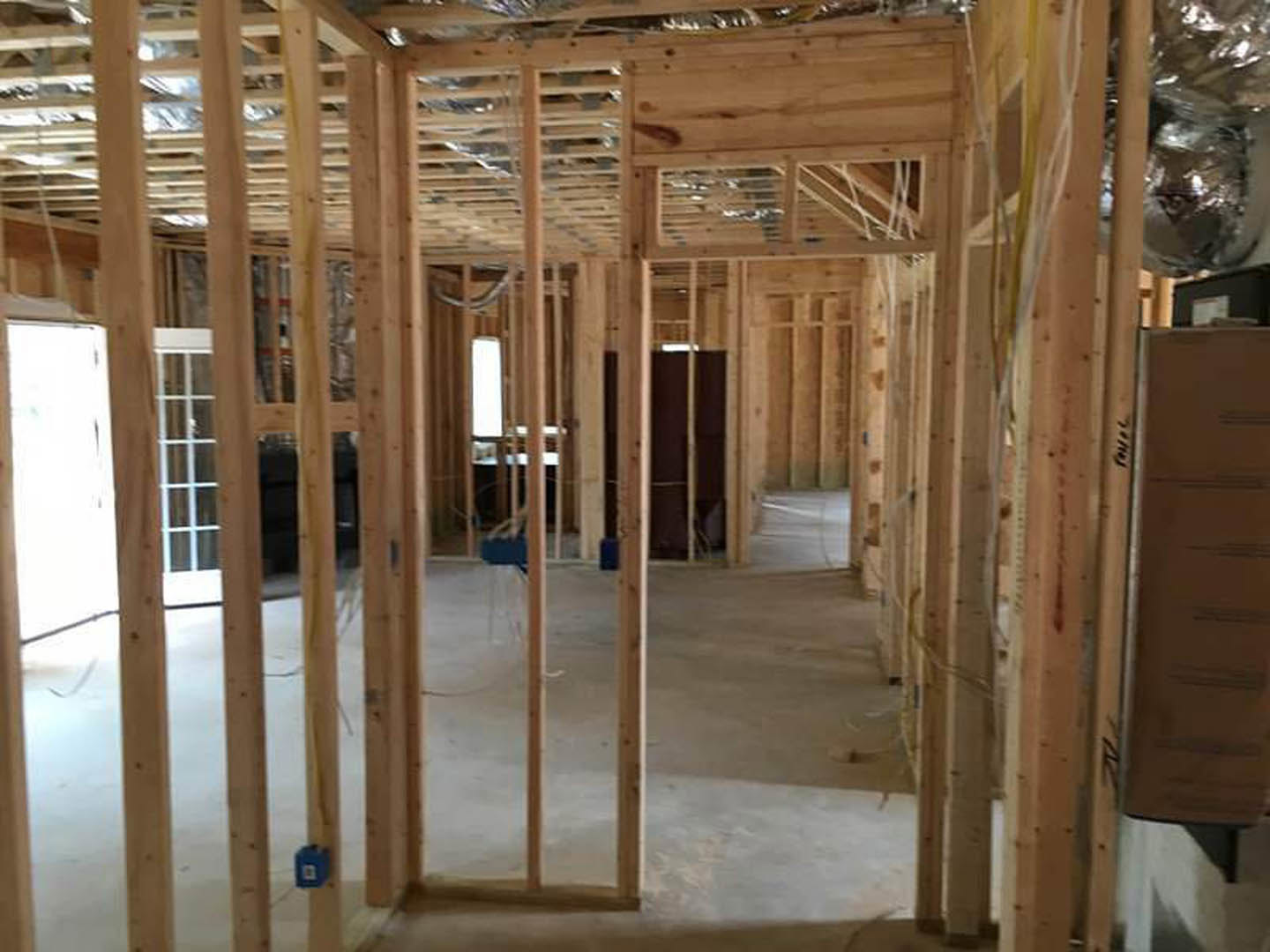 Exposed wood framing with beams and planks, unfinished ceiling and floor, construction materials visible in background