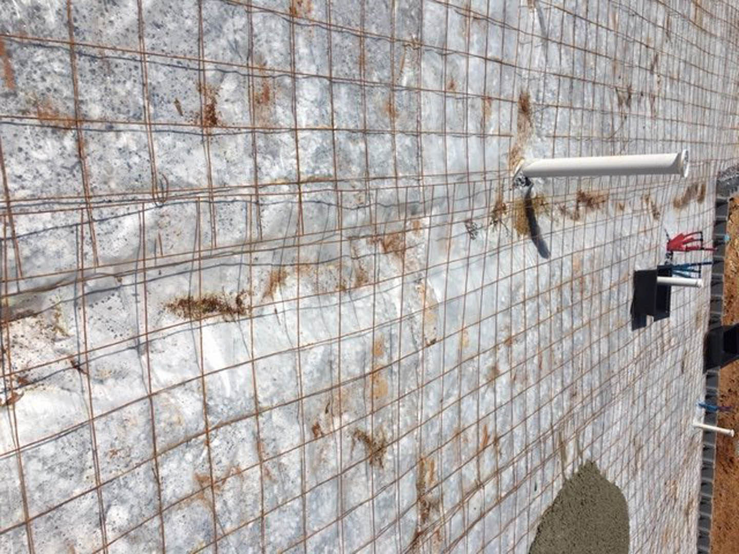 White plastic sheet covering wire mesh and cement wall, white pipe running vertically with brick and concrete finishes in the background.