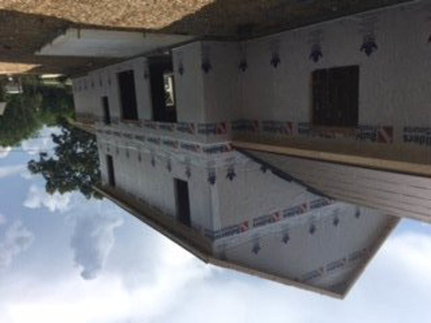Partially built house with exposed framing, surrounded by trees under a cloudy sky