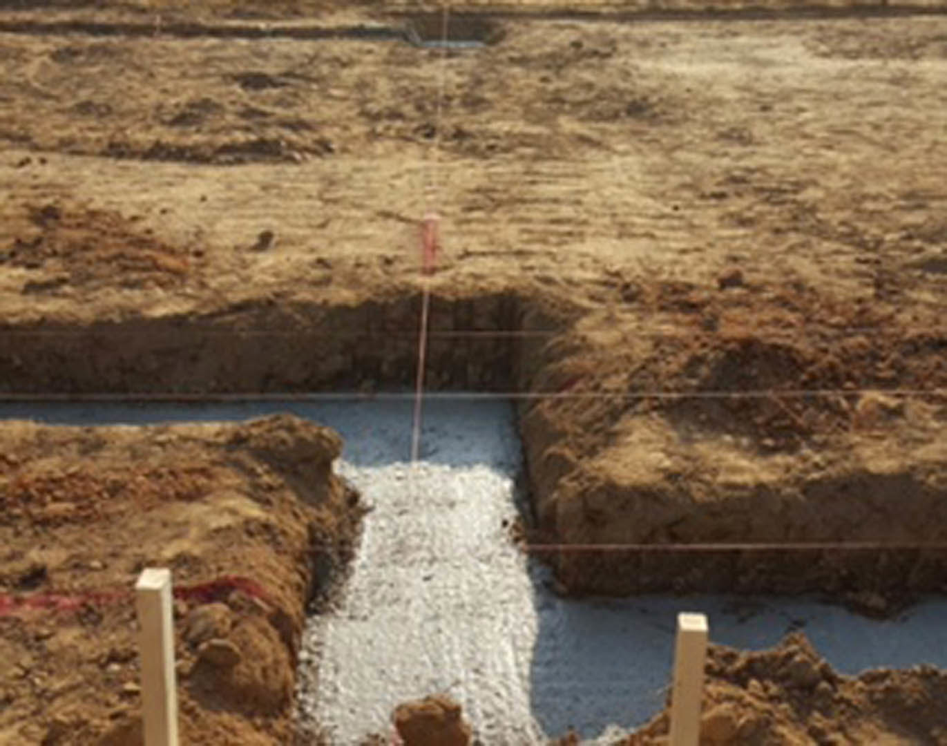 Excavated hole in dirt with scattered rocks and uneven ground, outdoor construction site