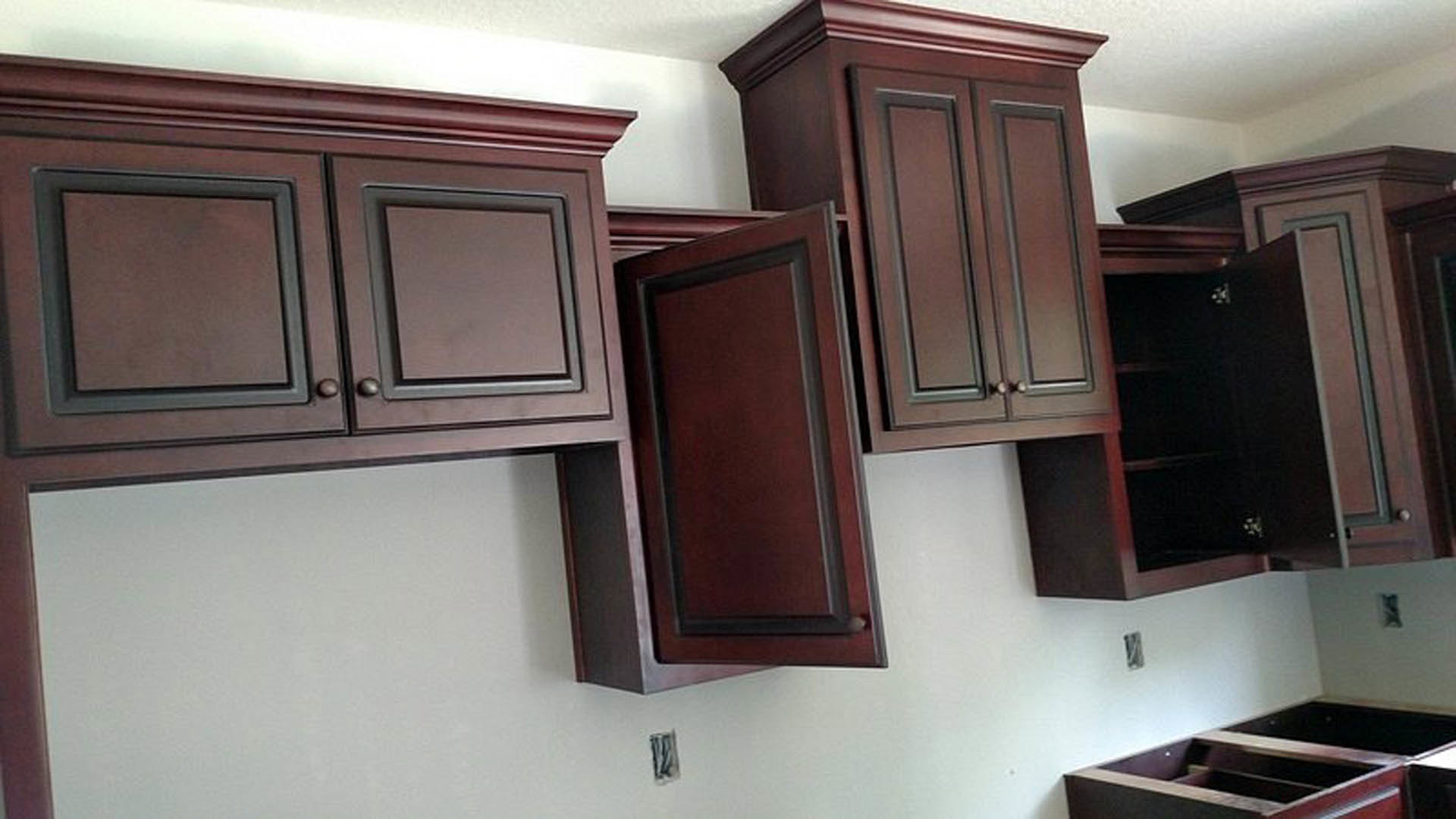 White kitchen cabinets with open doors revealing shelves, stainless steel appliances, brown cabinet fronts, wall outlet, and metal hardware.
