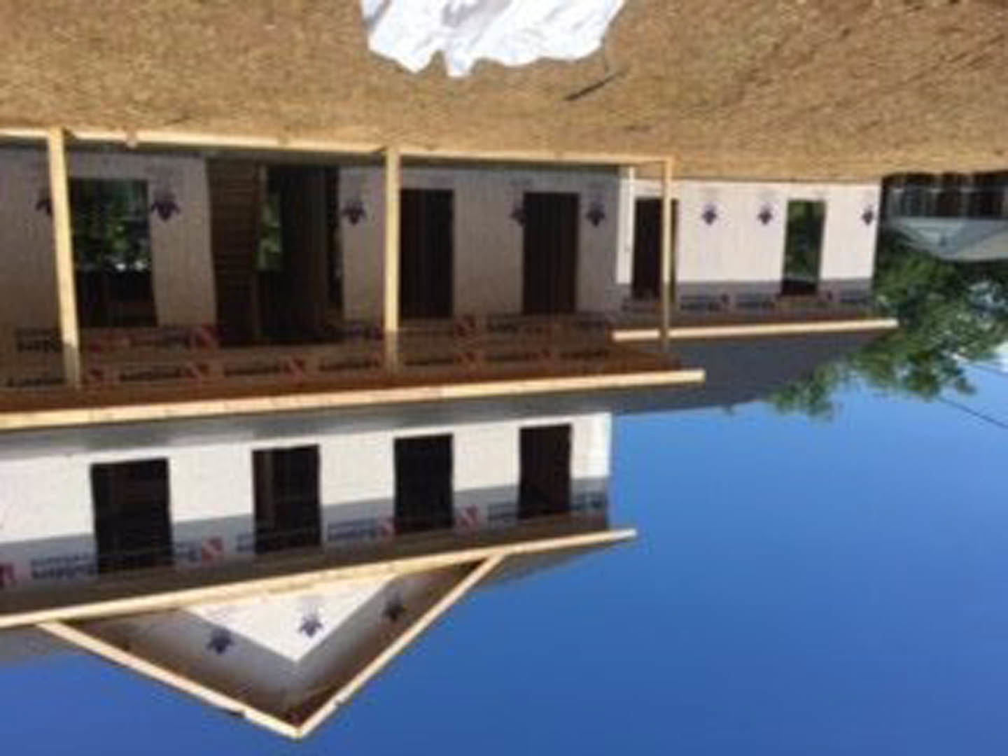 Modern house with large windows and triangular roof, reflected in calm water, surrounded by natural landscaping