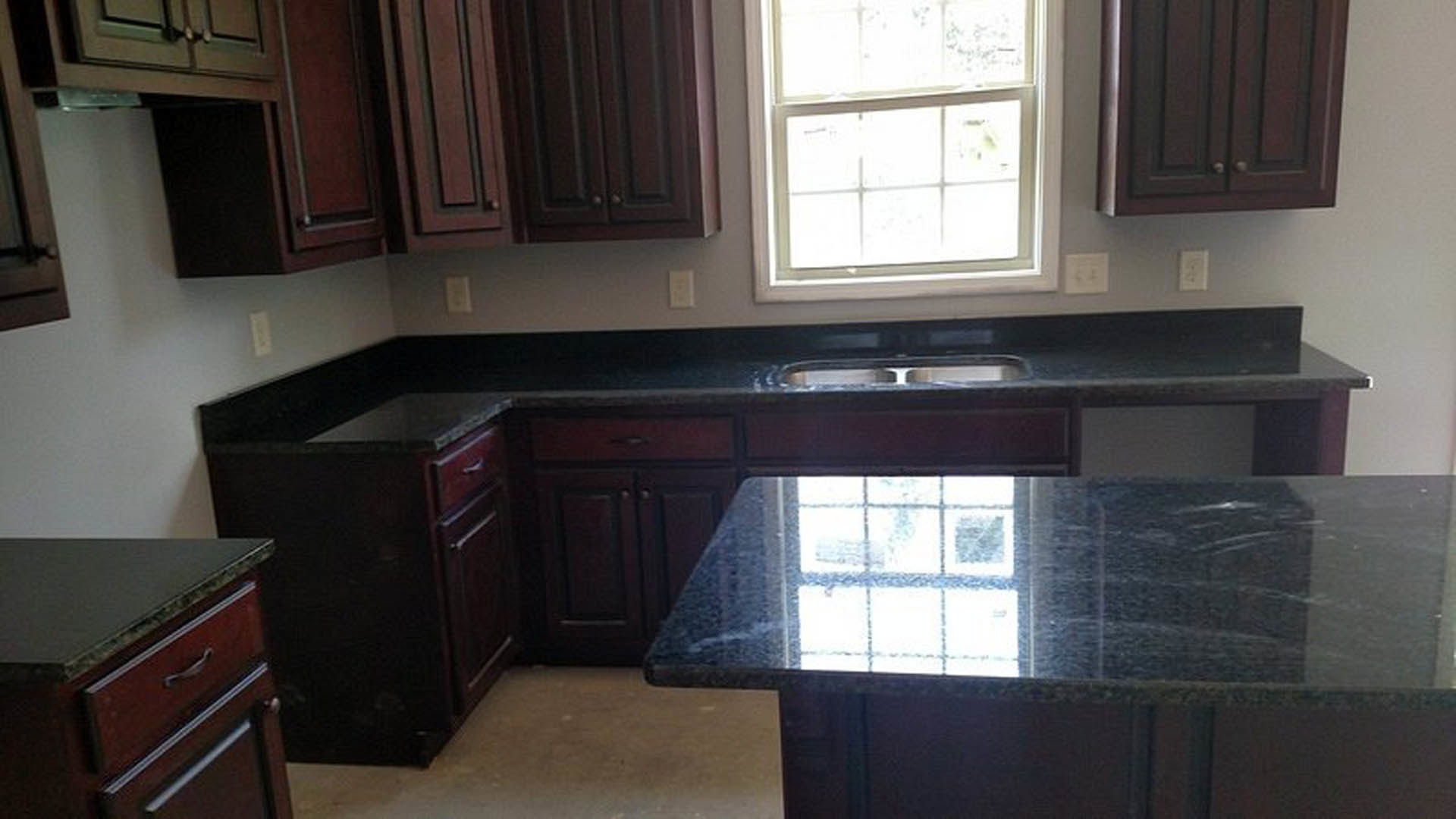 Dark wood kitchen cabinets with brushed metal handles, white-framed window letting in natural light, white electrical outlet on the wall, countertop with stainless steel sink, and
