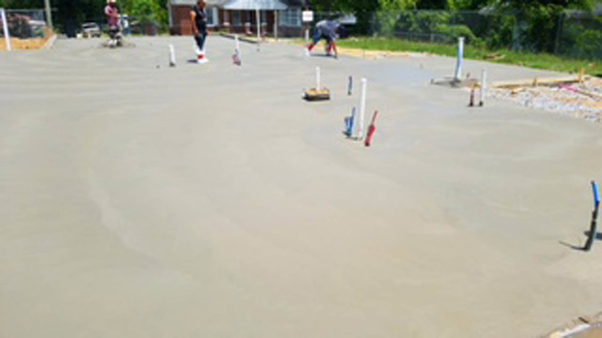 Modern custom home exterior with large windows, surrounded by trees and landscaped grounds; group of people playing cricket on outdoor lawn.