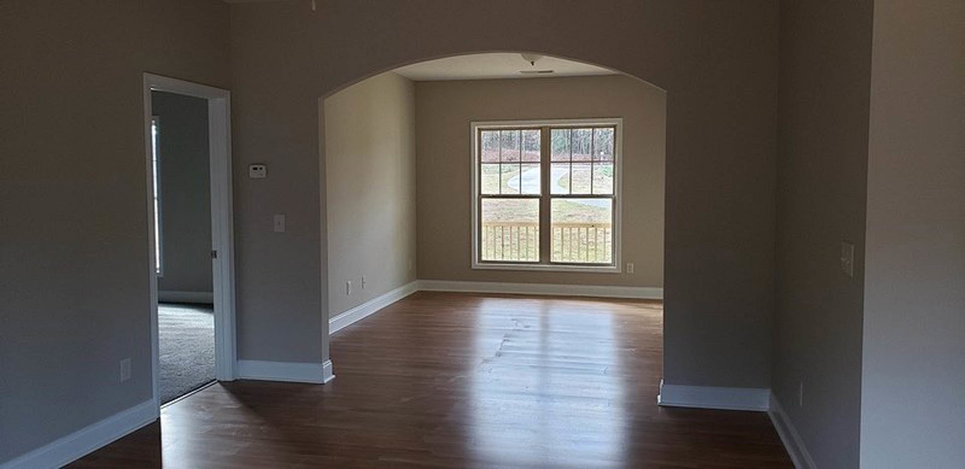 Hardwood floor with white baseboards, large window overlooking street, neutral painted walls