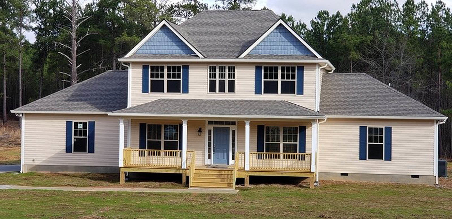 Wooden porch with white railing, blue front door with white trim, white-framed window, light-colored siding, surrounded by trees
