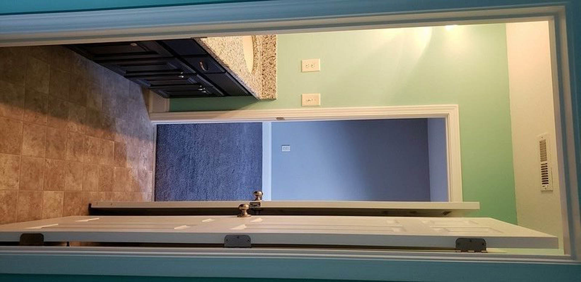 Blue bathroom wall with white border, wooden door frame, white outlet with black buttons, and light switch partially visible.