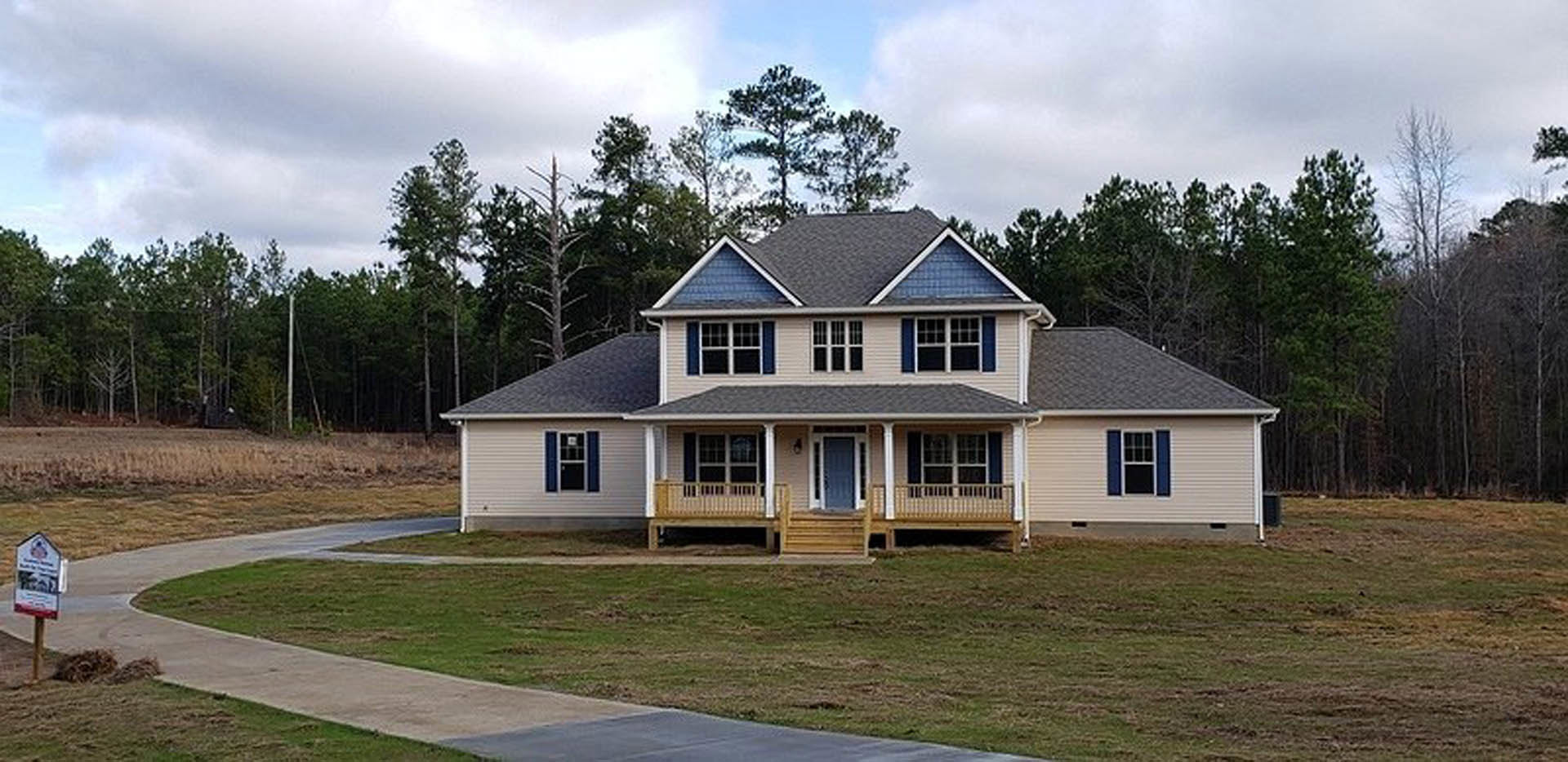 Two-story house with blue front door, white trim, multi-pane windows, covered porch, manicured lawn, and mature trees in the background
