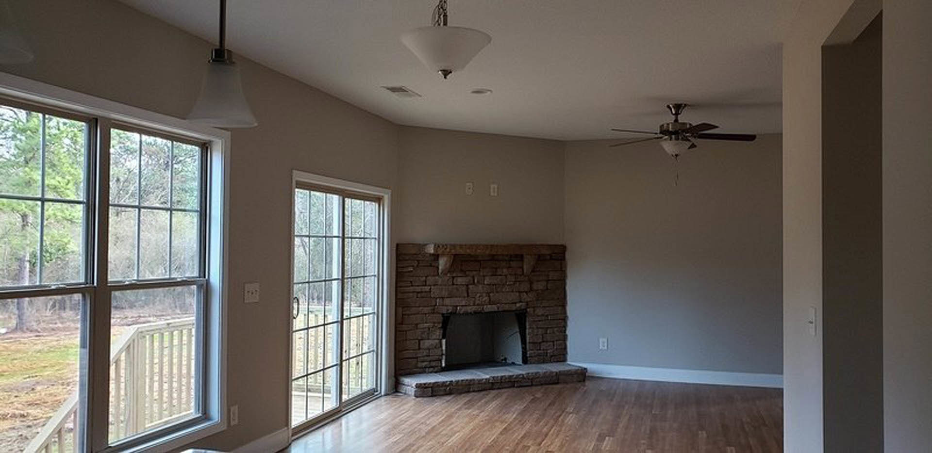 Living room featuring stone fireplace, ceiling fan with light fixture, hardwood floors, large windows, and neutral painted walls