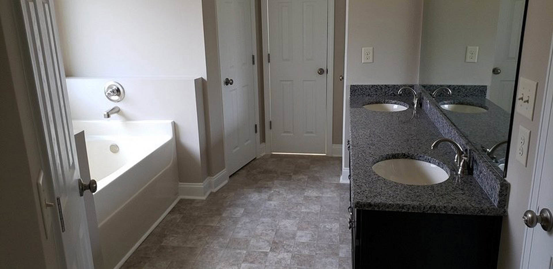 Bathroom with marble countertops, white tile walls, built-in sink, chrome faucet, wall-mounted mirror, and a close-up of a white electrical outlet near the bathtub.