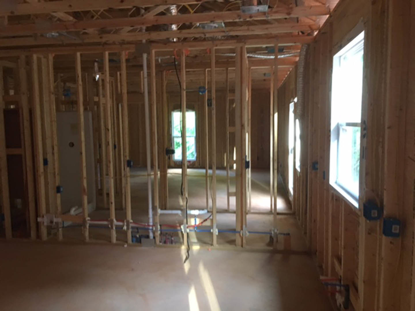 Living room with exposed wood ceiling beams, large windows letting in daylight, white door, and light-colored flooring