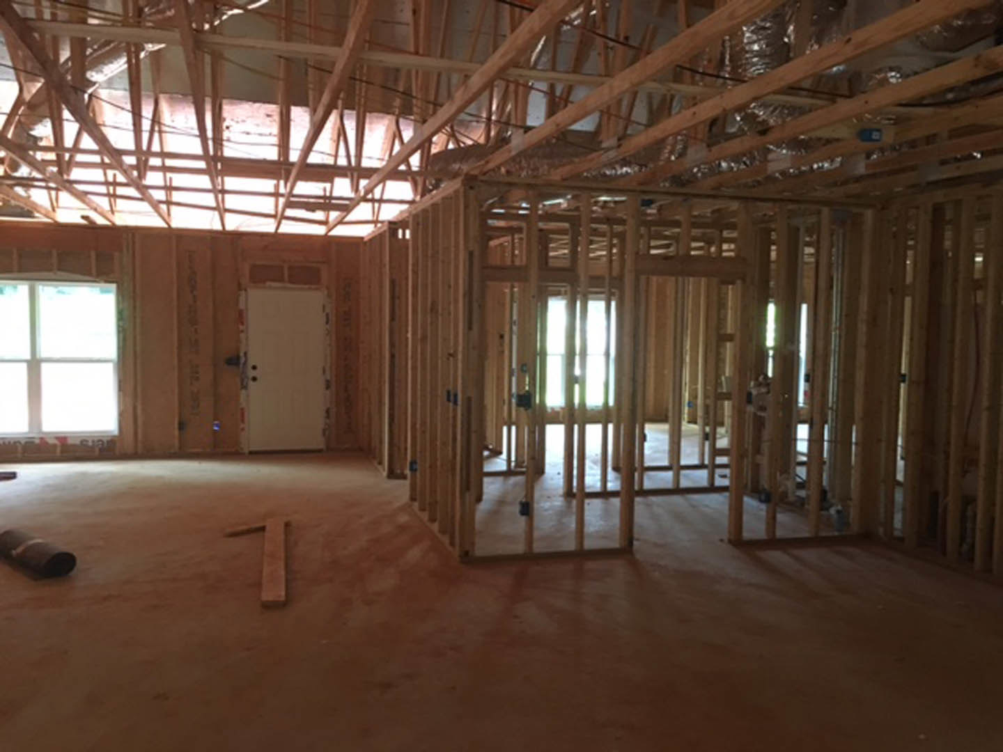 Wood-framed room with exposed ceiling beams, white door with black knobs, brown door with square frame, close-up window, and roll of insulation paper on unfinished floor
