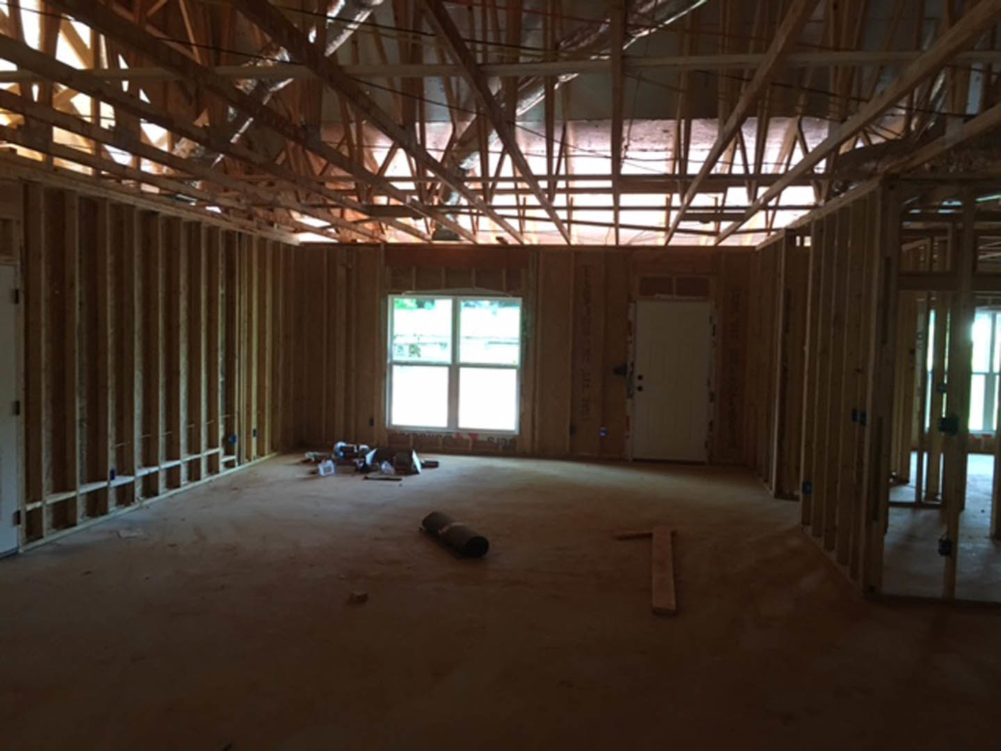 White-framed window and white door with black handle in a room featuring exposed ceiling beams, unfinished flooring, and a roll of carpet.