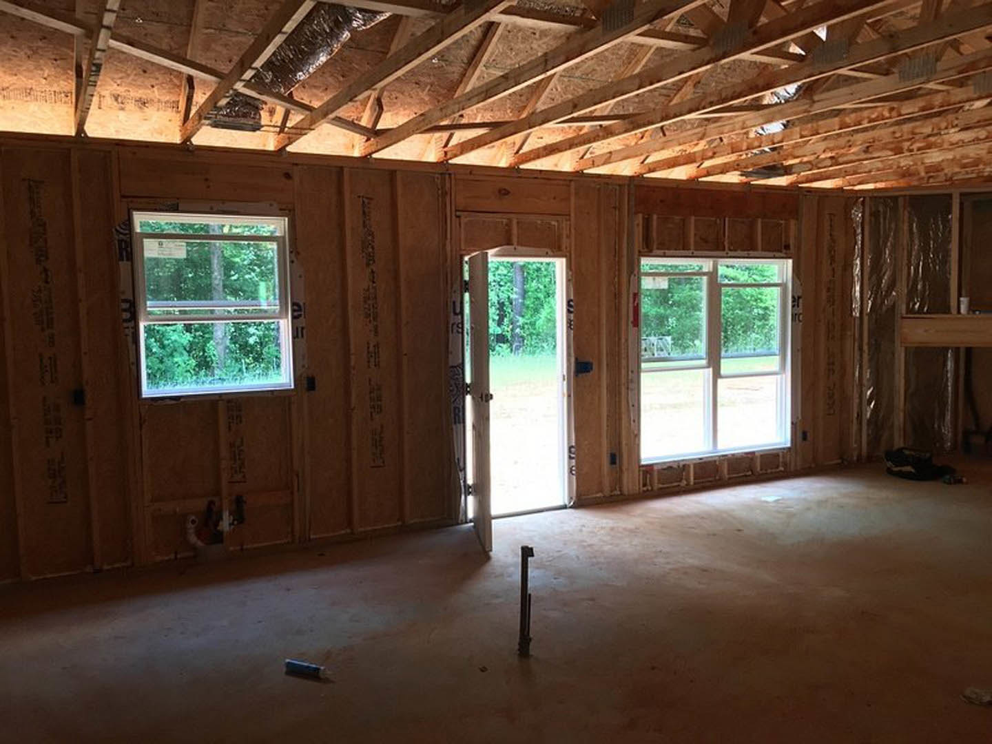 Spacious room with light wood flooring, exposed wooden ceiling beams, large white-framed windows, and double glass doors opening to a grassy yard