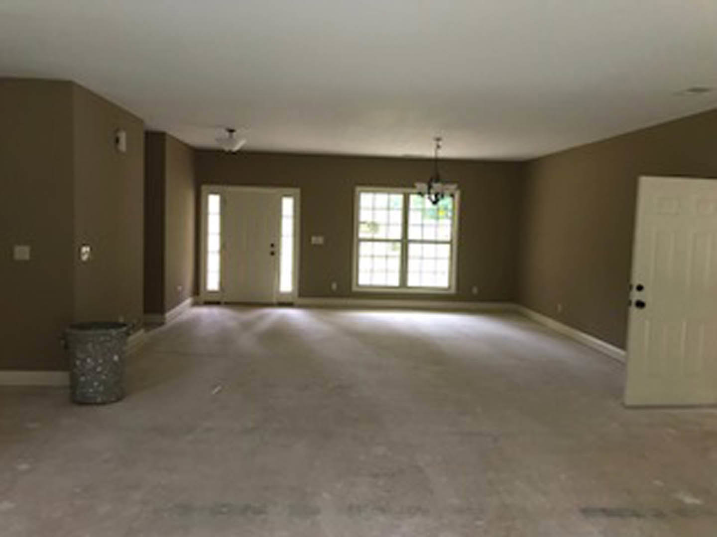 Bright room with white walls, white door featuring black knobs, large windows, light wood flooring, and sunlight streaming across the floor.