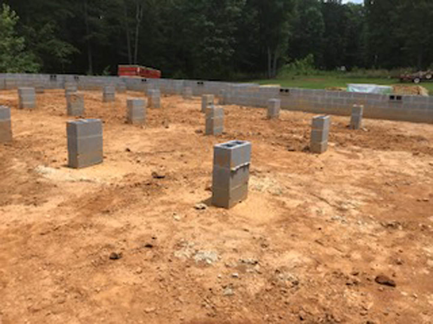 Concrete block foundation set in dirt, surrounded by soil and scattered trees in the background