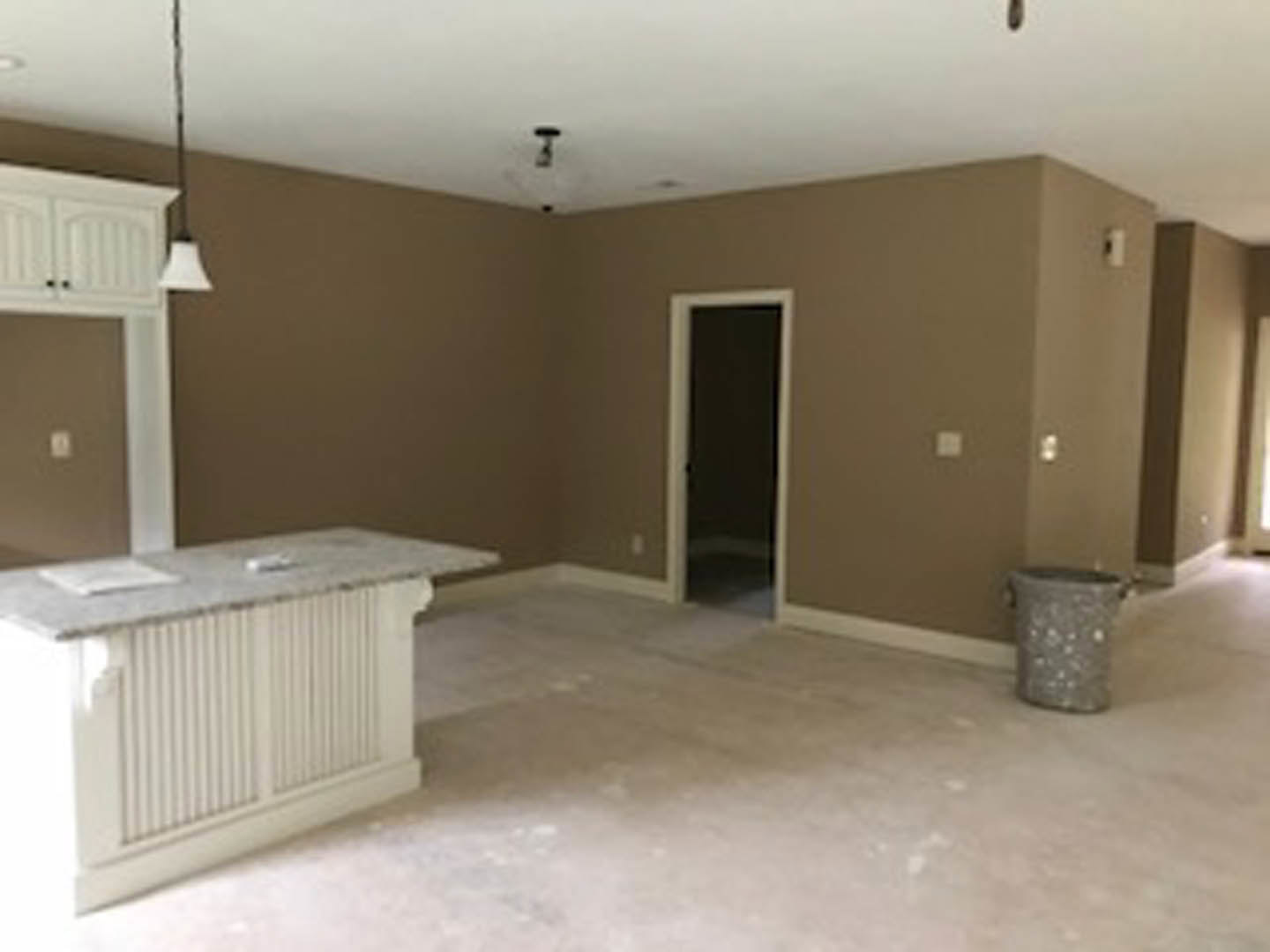 Kitchen with white marble countertop, stainless steel sink, light tile flooring, grey trash can beside cabinetry, open door leading to adjacent room