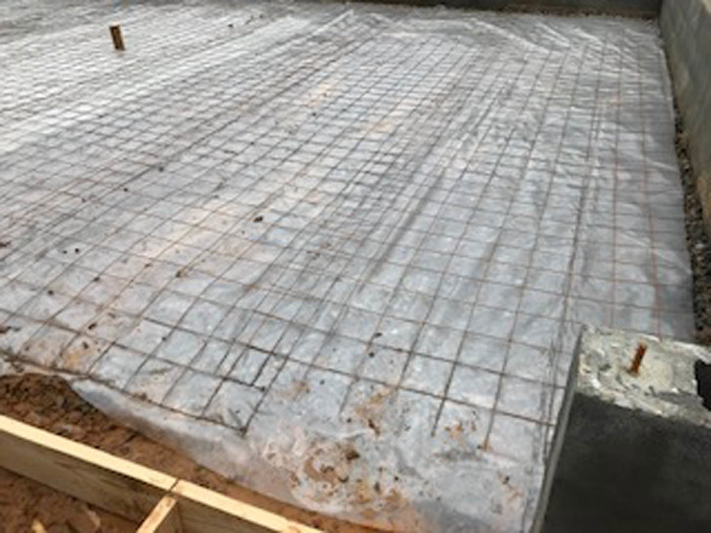 Metal rebar grid laid over concrete foundation at outdoor residential construction site