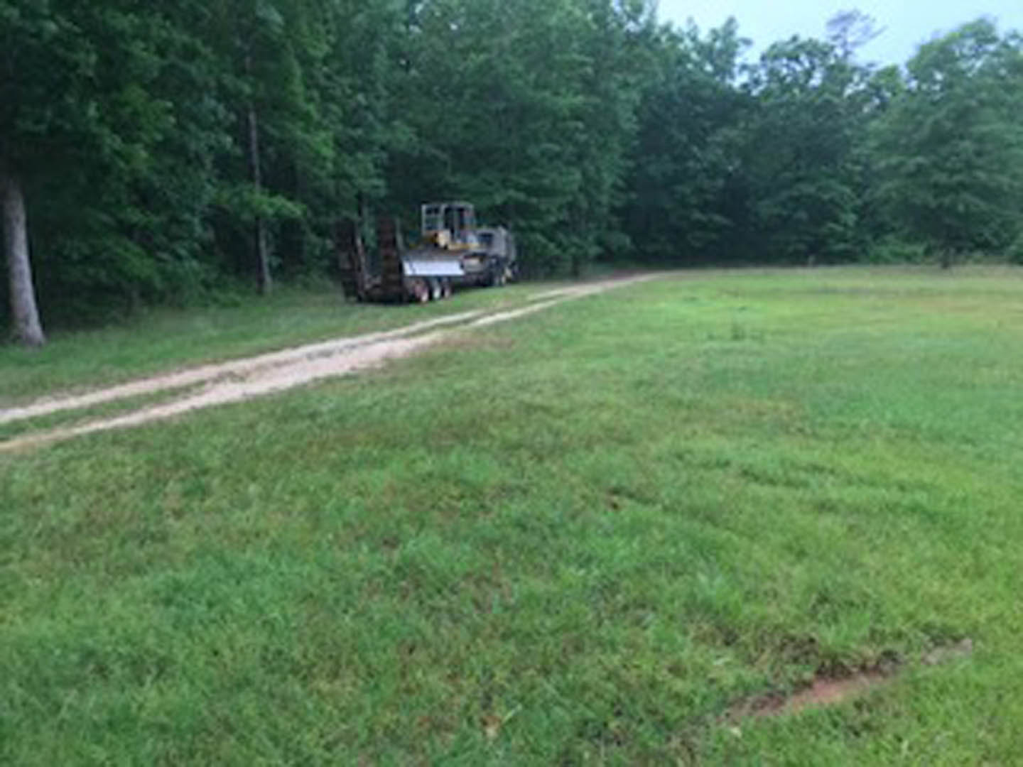 Tractor parked on a dirt road surrounded by grassy field and trees, under a clear sky