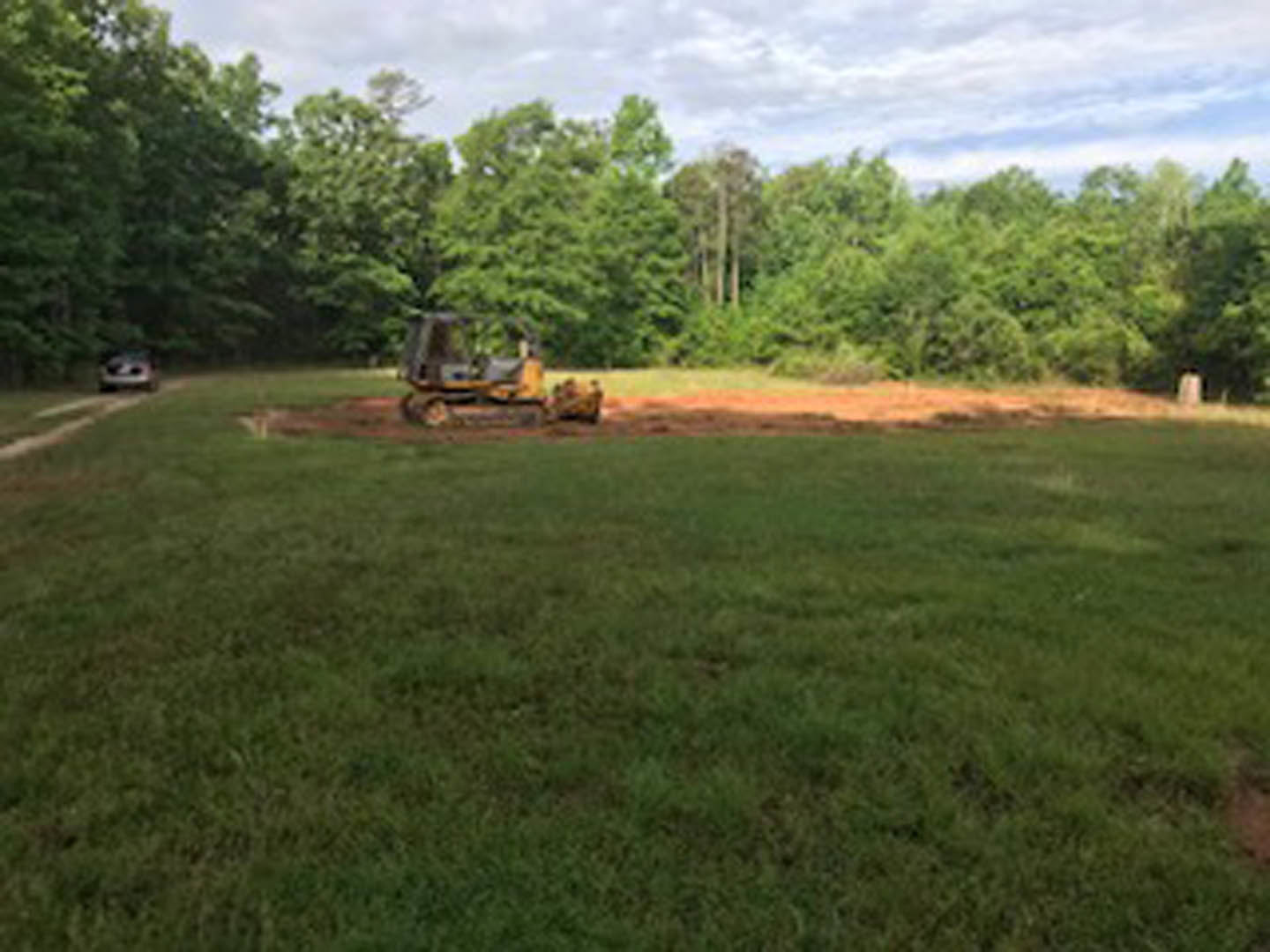 Bulldozer parked on grassy field with scattered trees and cloudy sky in background