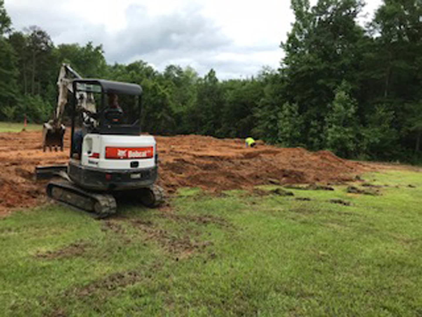 White and black bulldozer parked on dirt field surrounded by grass and trees under cloudy sky