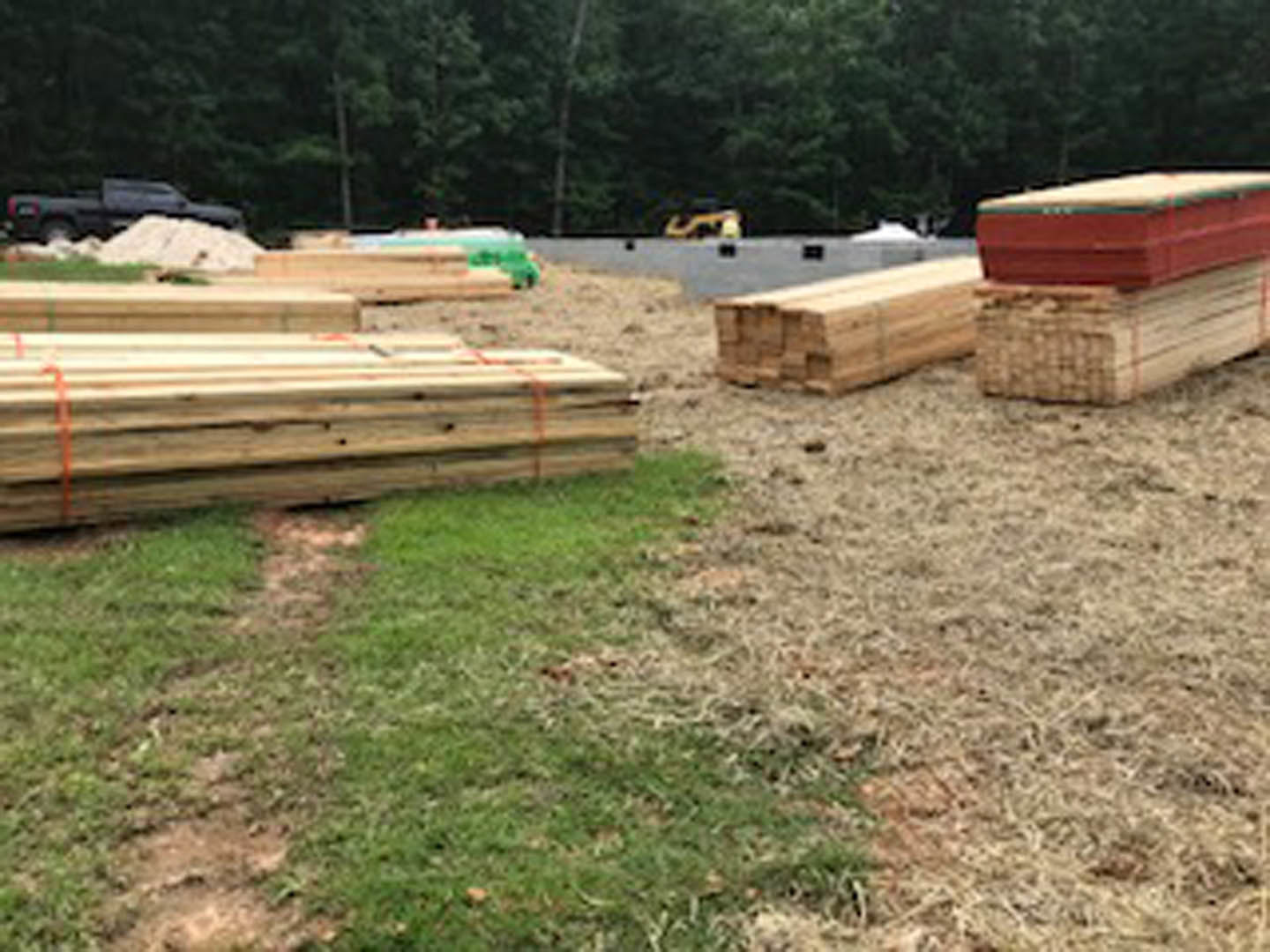 Stack of wooden planks resting on green grass near trees in an outdoor residential setting
