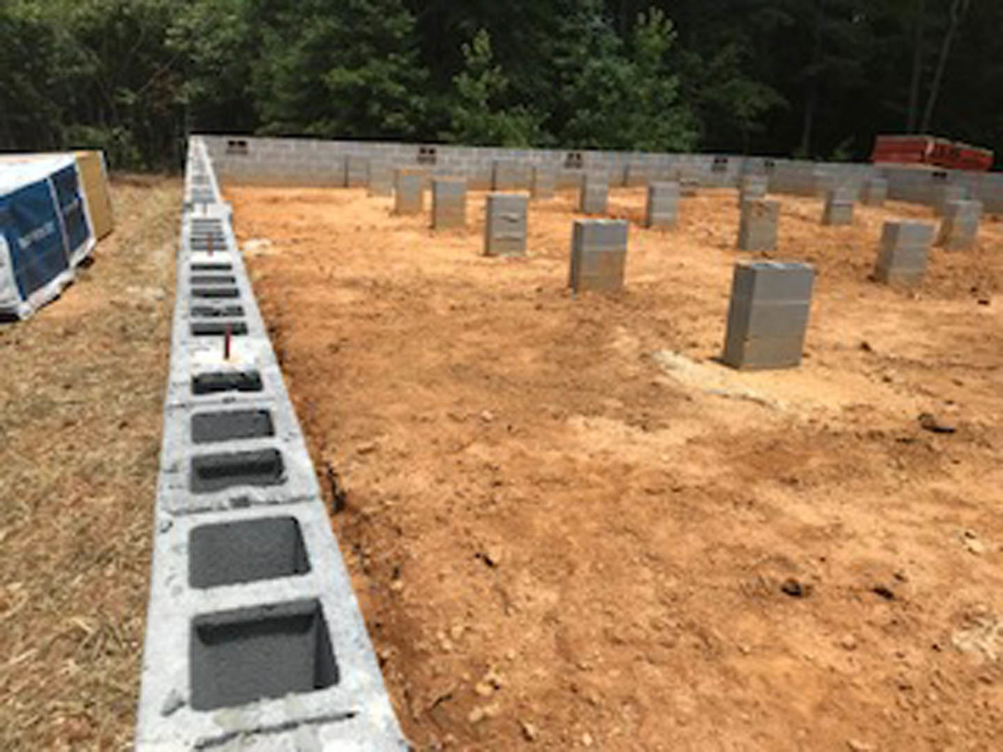 Concrete foundation with multiple square concrete blocks set in soil, surrounded by outdoor construction area and trees in background