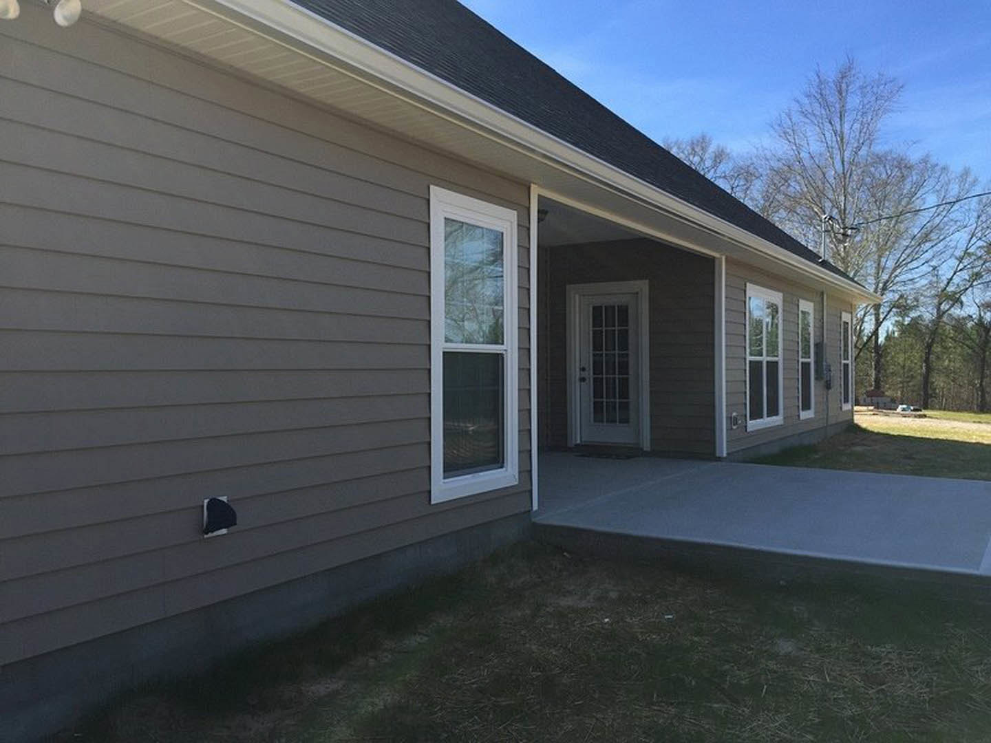 Two-story home with light siding, white garage door with glass panes, concrete driveway, covered porch, black wall-mounted fixture, and large windows.