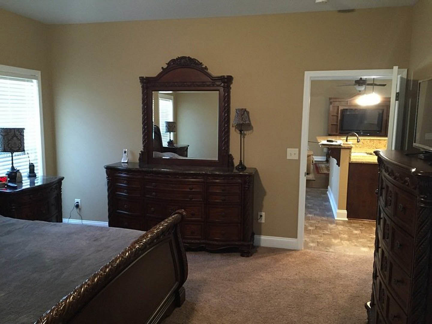 Bedroom with metal bed frame, wooden dresser with drawers, wall-mounted mirror, and lamp; hardwood flooring and neutral wall colors.