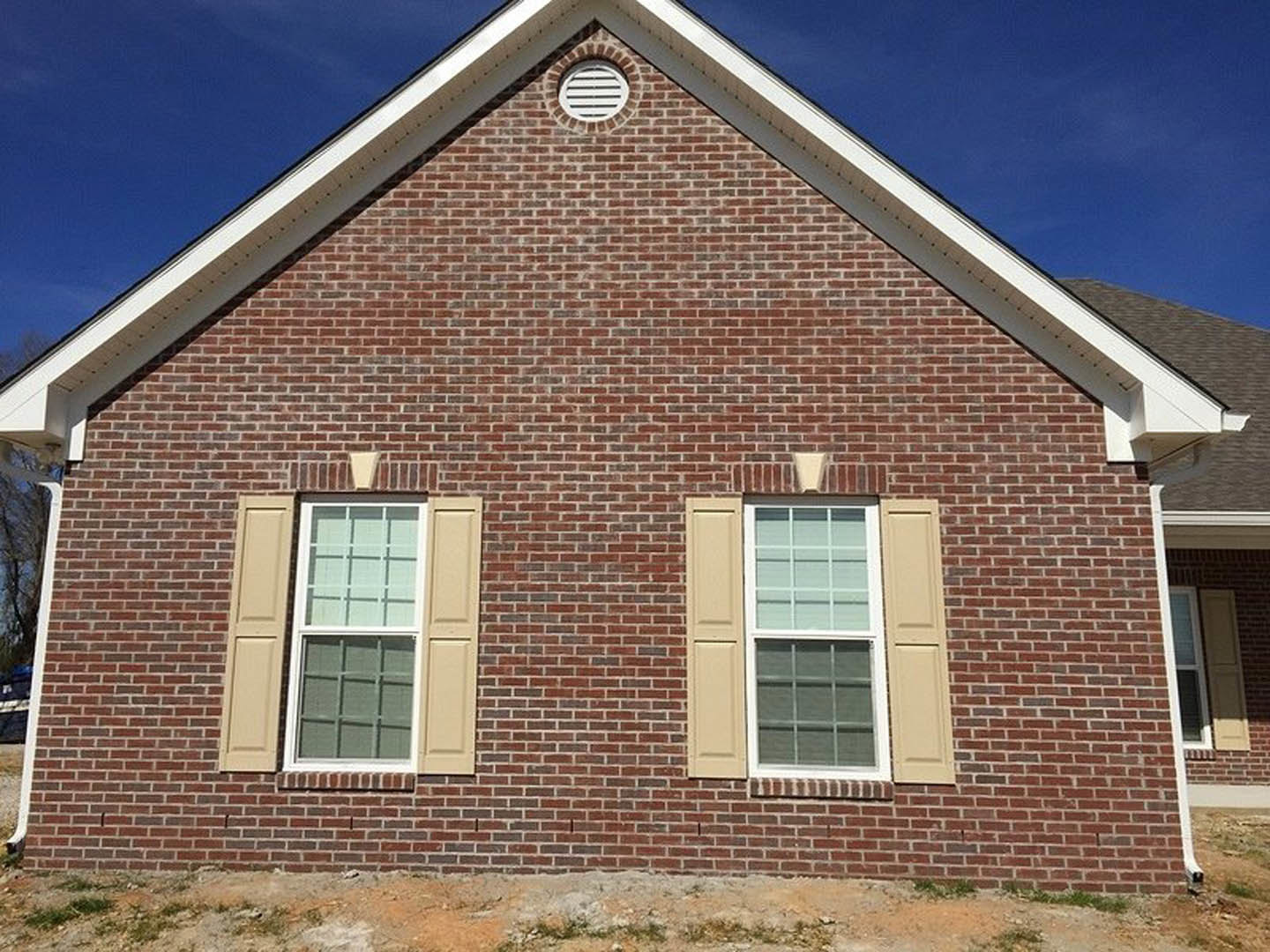 Red brick house with gabled roof, white-framed window, exterior vent, and grassy yard