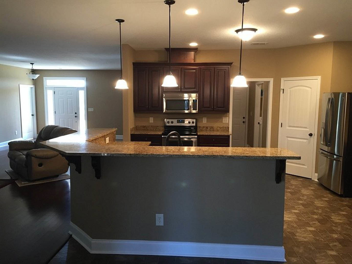 Open-concept kitchen and living room featuring a granite countertop bar, stainless steel refrigerator, open microwave, stove, cabinetry, sink, and a seating area with a couch and