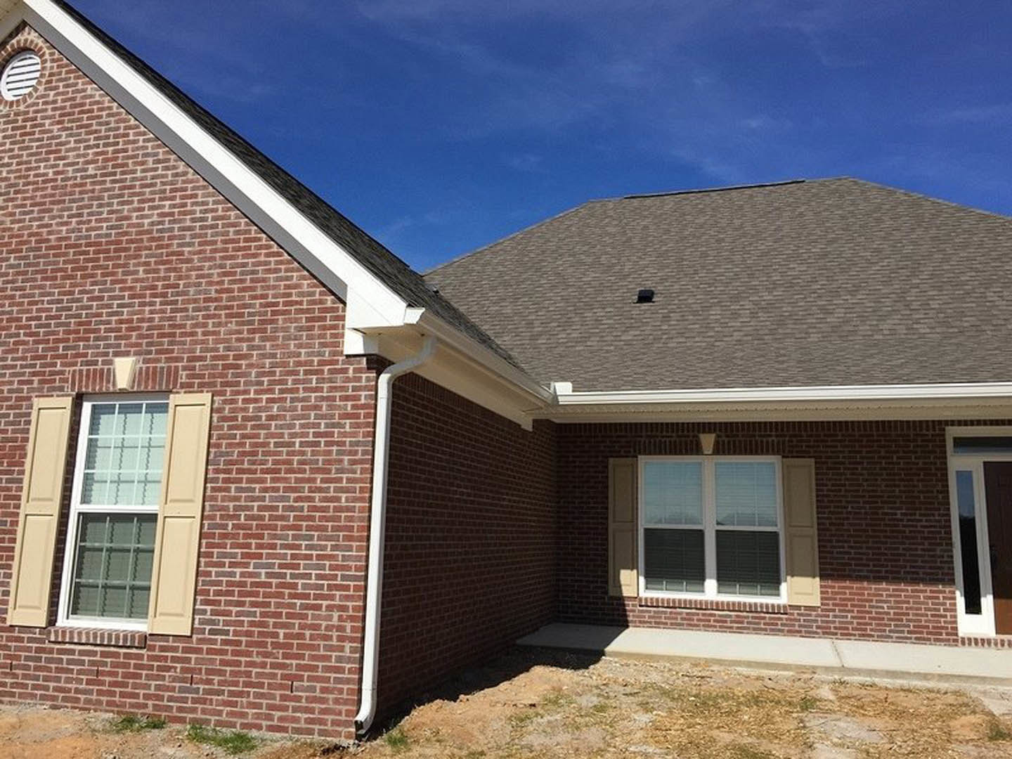 Red brick exterior with white roof, white-framed window with blinds, roof vent, and cloudy sky in background