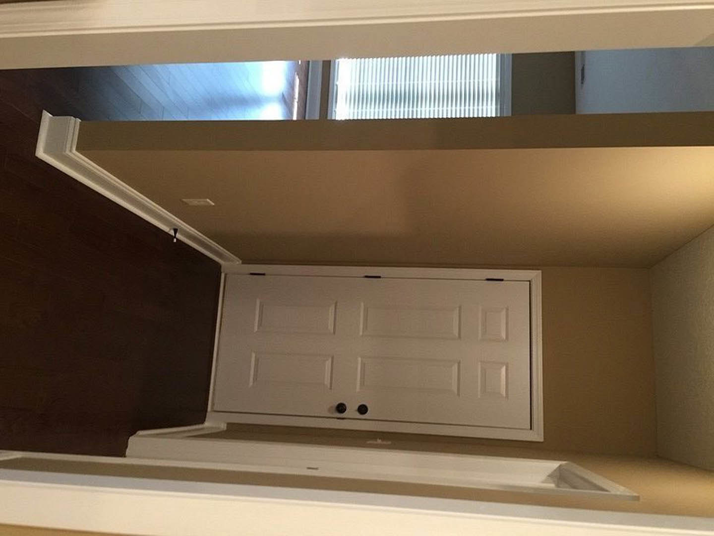 White paneled door in a hallway with white walls, crown molding, and a built-in cabinet featuring black knobs; window partially visible.